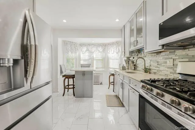 Kitchen featuring stainless steel appliances, white tile flooring, gray cabinetry, light-toned countertops, and a tiled backsplash Kitchen featuring stainless steel appliances, white tile flooring, gray cabinetry, light-toned countertops, and a tiled backsplash