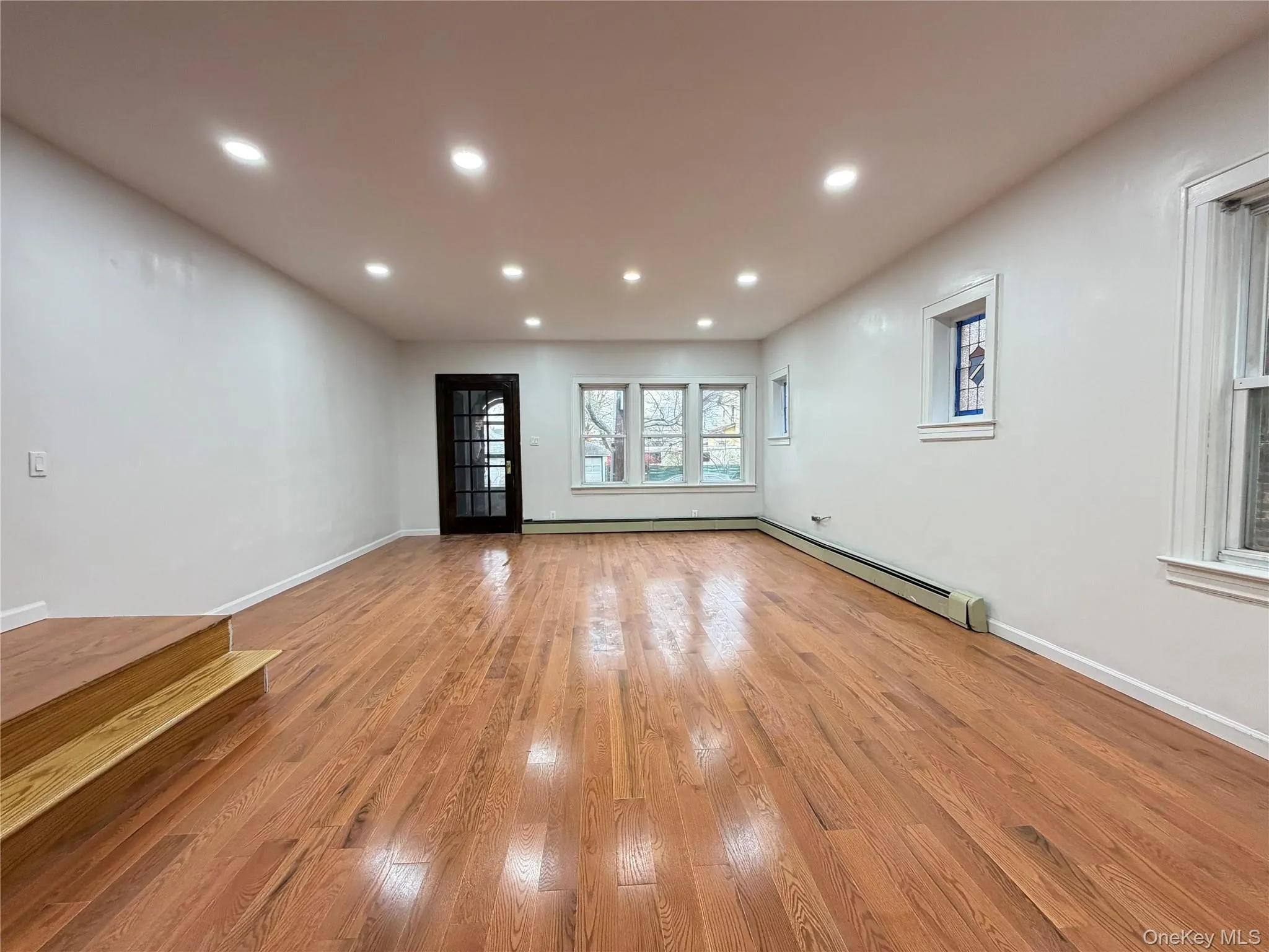 Unfurnished living room featuring light wood-style floors, recessed lighting, and baseboard heating Unfurnished living room featuring light wood-style floors, recessed lighting, and baseboard heating