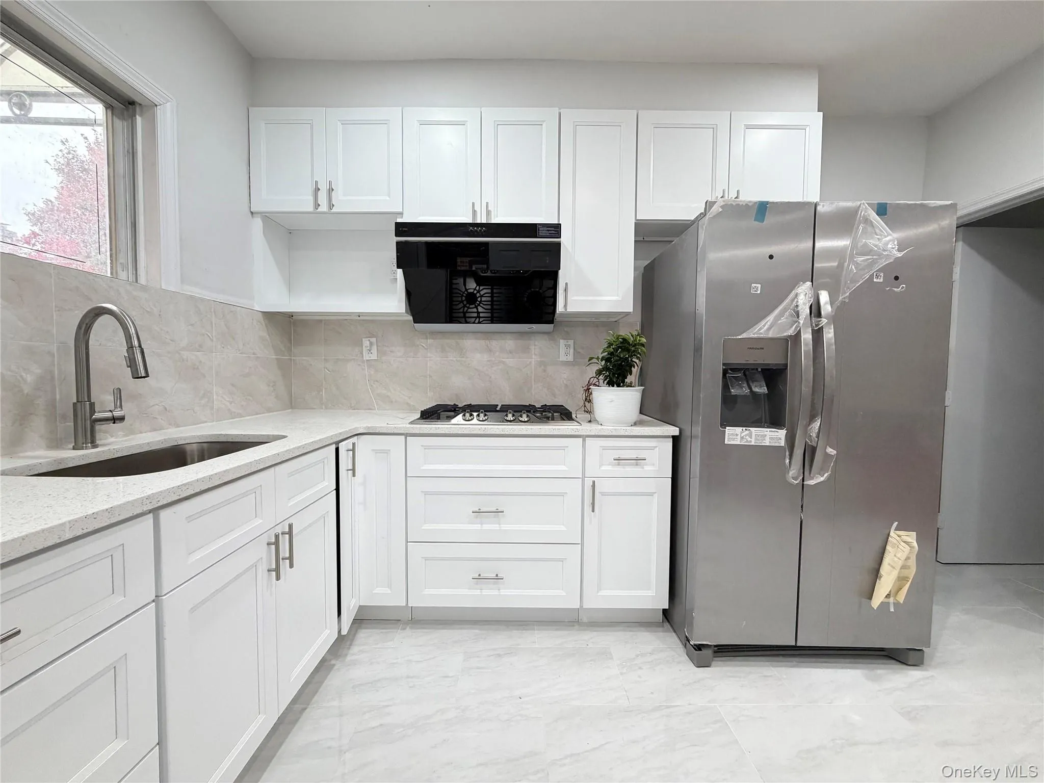 Kitchen featuring stainless steel fridge with ice dispenser, backsplash, white cabinetry, light stone countertops, and black microwave Kitchen featuring stainless steel fridge with ice dispenser, backsplash, white cabinetry, light stone countertops, and black microwave