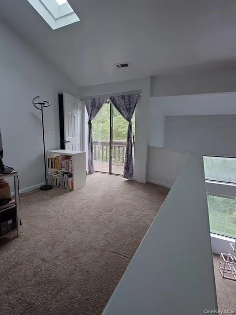 Living room featuring carpet floors, a skylight, and baseboards Living room featuring carpet floors, a skylight, and baseboards