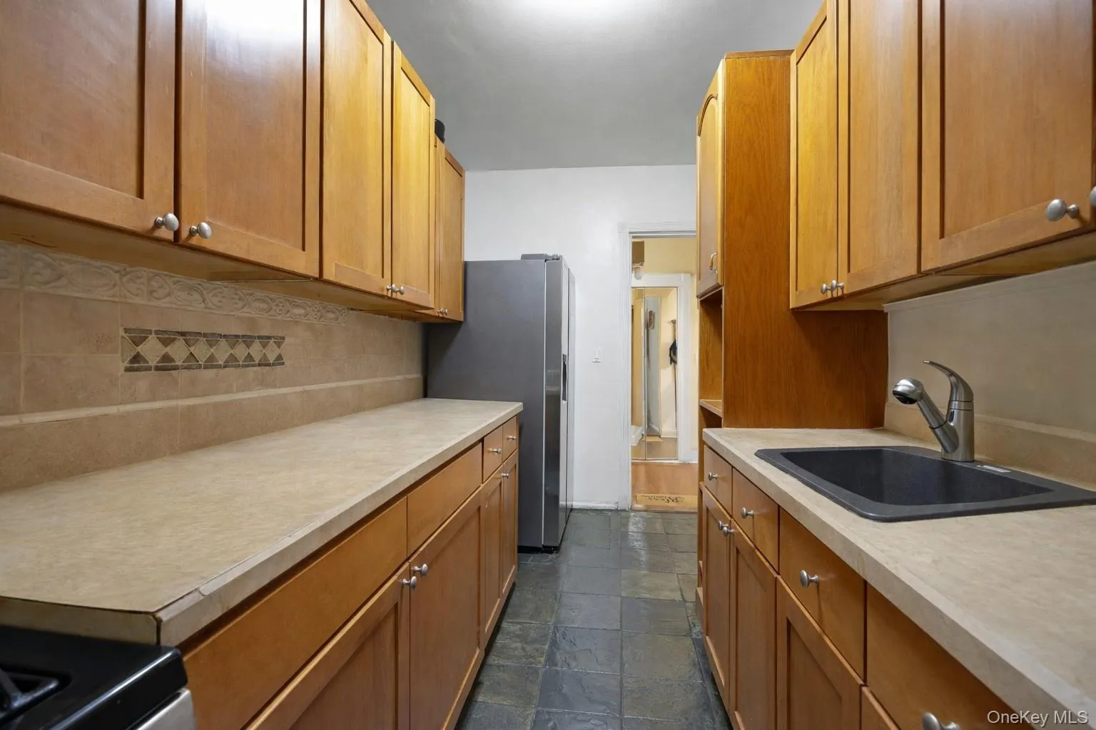 Kitchen featuring light countertops, dark stone finish floors, freestanding refrigerator, and wood finish cabinets Kitchen featuring light countertops, dark stone finish floors, freestanding refrigerator, and wood finish cabinets