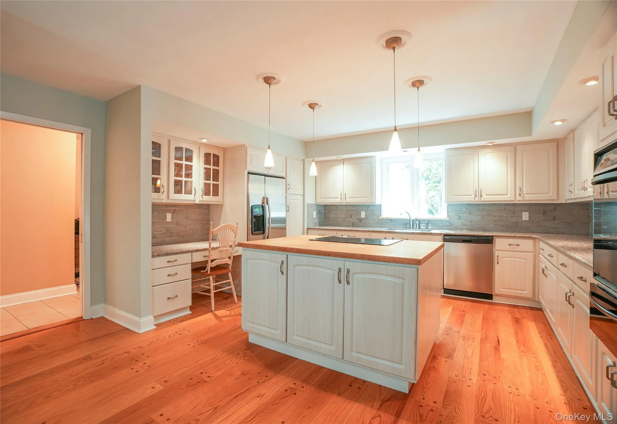 Gourmet kitchen featuring wood-finish flooring, white cabinetry, an island with a wood countertop, stainless steel appliances, and a built-in desk area Gourmet kitchen featuring wood-finish flooring, white cabinetry, an island with a wood countertop, stainless steel appliances, and a built-in desk area
