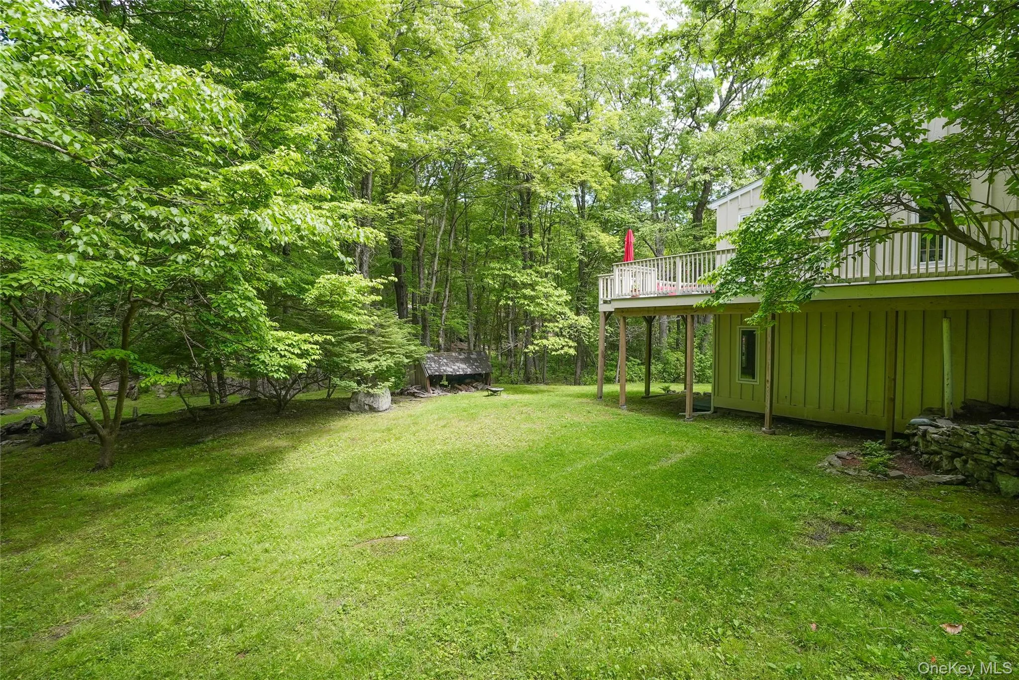 Expansive green lawn surrounded by mature trees, featuring a raised outdoor deck with white railings Expansive green lawn surrounded by mature trees, featuring a raised outdoor deck with white railings