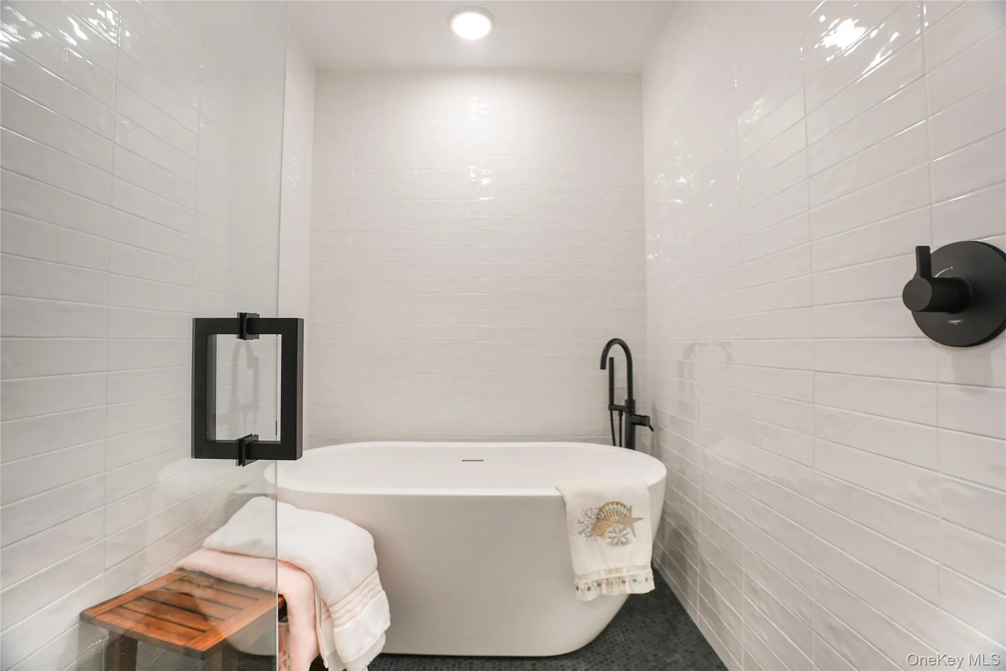 Freestanding soaking tub with matte black floor-mounted filler, complemented by white horizontal subway tile walls and dark tile flooring Freestanding soaking tub with matte black floor-mounted filler, complemented by white horizontal subway tile walls and dark tile flooring