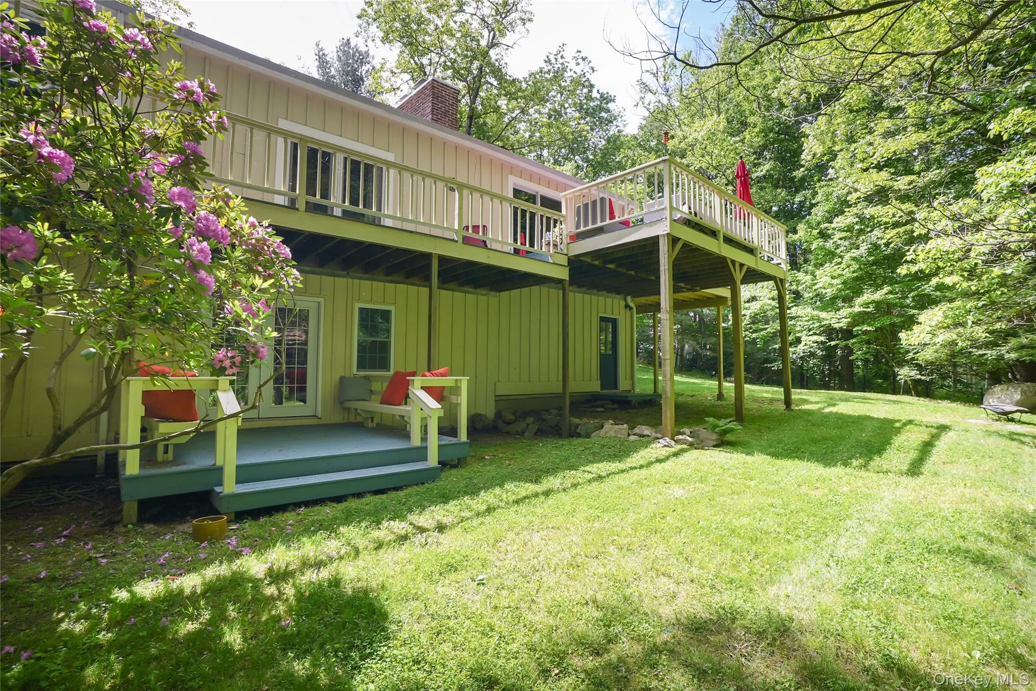 Expansive rear yard featuring a large elevated wood deck with railing, a ground-level wood deck, a brick chimney, and mature trees Expansive rear yard featuring a large elevated wood deck with railing, a ground-level wood deck, a brick chimney, and mature trees