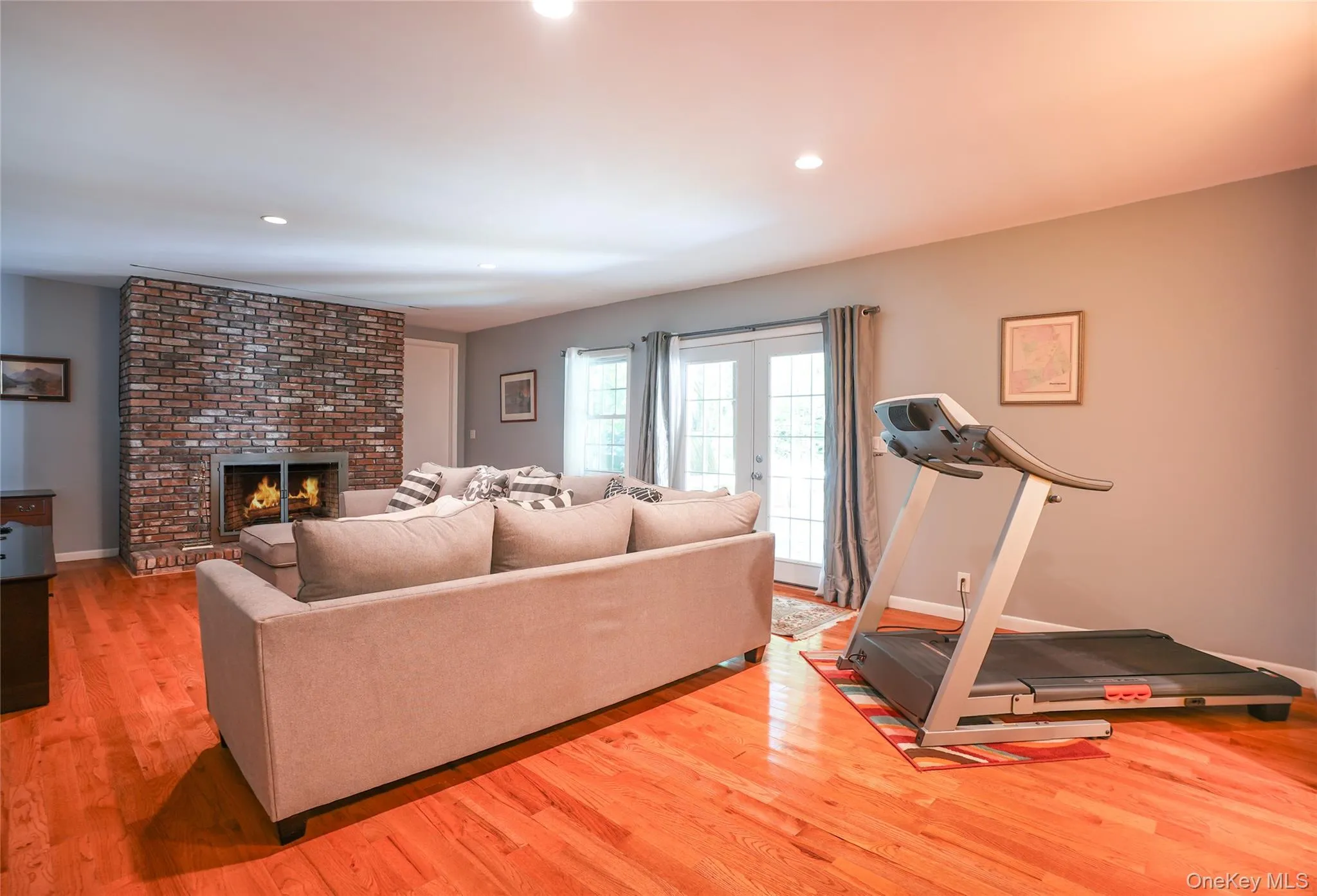 Living area featuring wood-finish flooring, a brick fireplace with a metal insert, recessed lighting, and French doors Living area featuring wood-finish flooring, a brick fireplace with a metal insert, recessed lighting, and French doors