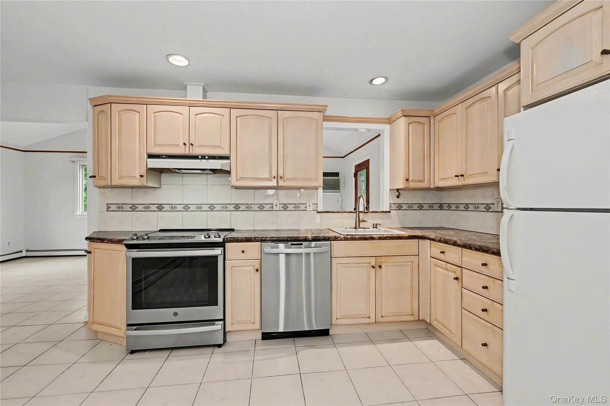 Kitchen featuring light wood cabinetry, stainless steel range, stainless steel dishwasher, tile flooring, and granite countertops. The pass through goes into the family room. Kitchen featuring light wood cabinetry, stainless steel range, stainless steel dishwasher, tile flooring, and granite countertops. The pass through goes into the family room.