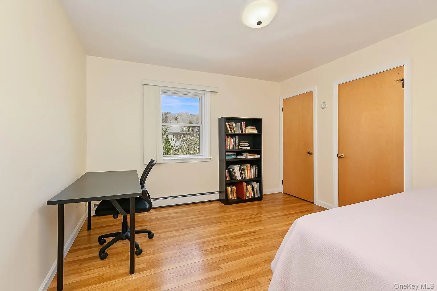Hardwood-style flooring throughout this room, featuring a window with natural light, two wood-paneled doors, and a ceiling-mounted light fixture Hardwood-style flooring throughout this room, featuring a window with natural light, two wood-paneled doors, and a ceiling-mounted light fixture