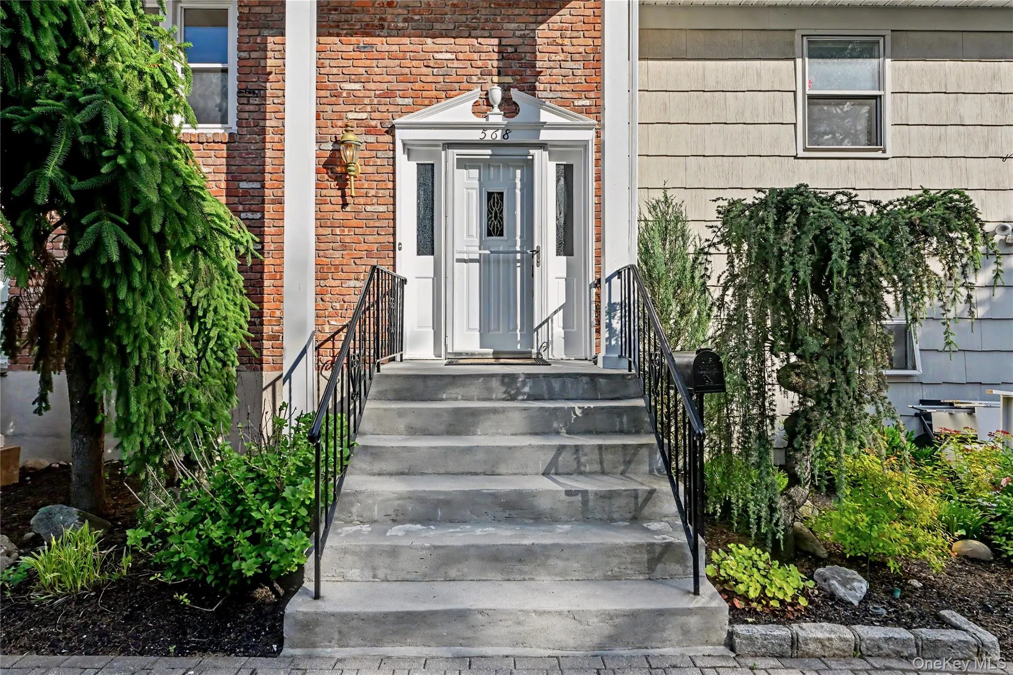 Front entry featuring concrete steps with wrought iron railings, a white front door with sidelights, and a brick facade Front entry featuring concrete steps with wrought iron railings, a white front door with sidelights, and a brick facade