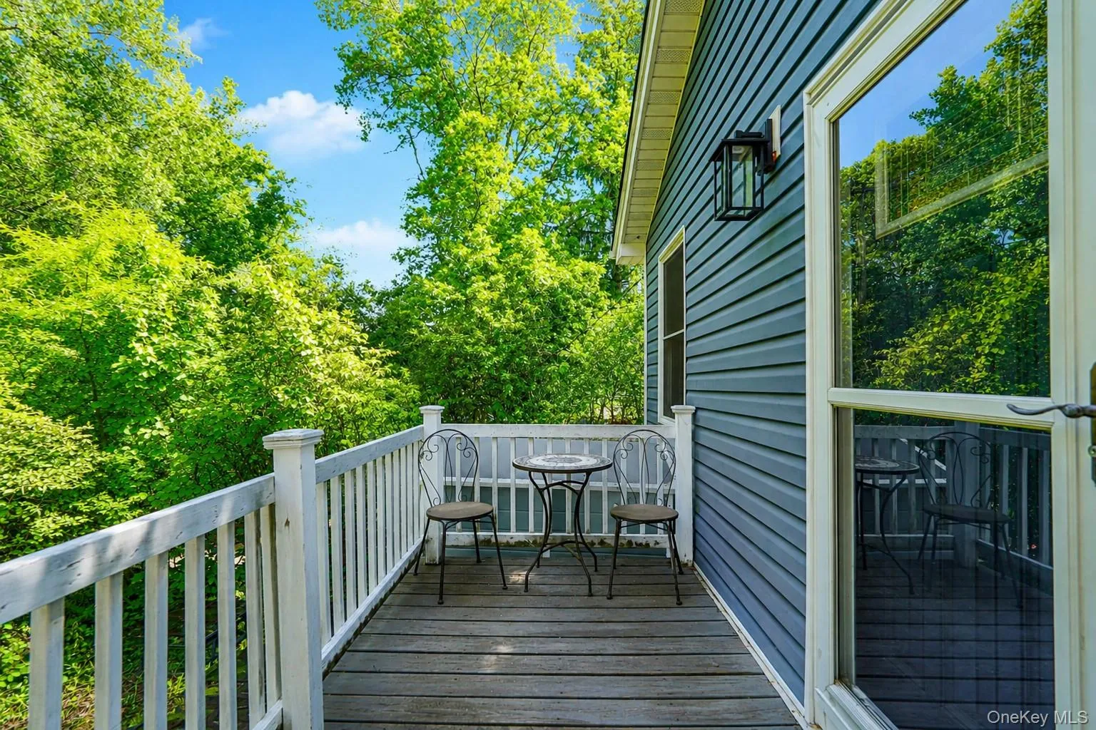 Exterior deck featuring wood-finish flooring, white railing, and a black wall-mounted lantern Exterior deck featuring wood-finish flooring, white railing, and a black wall-mounted lantern