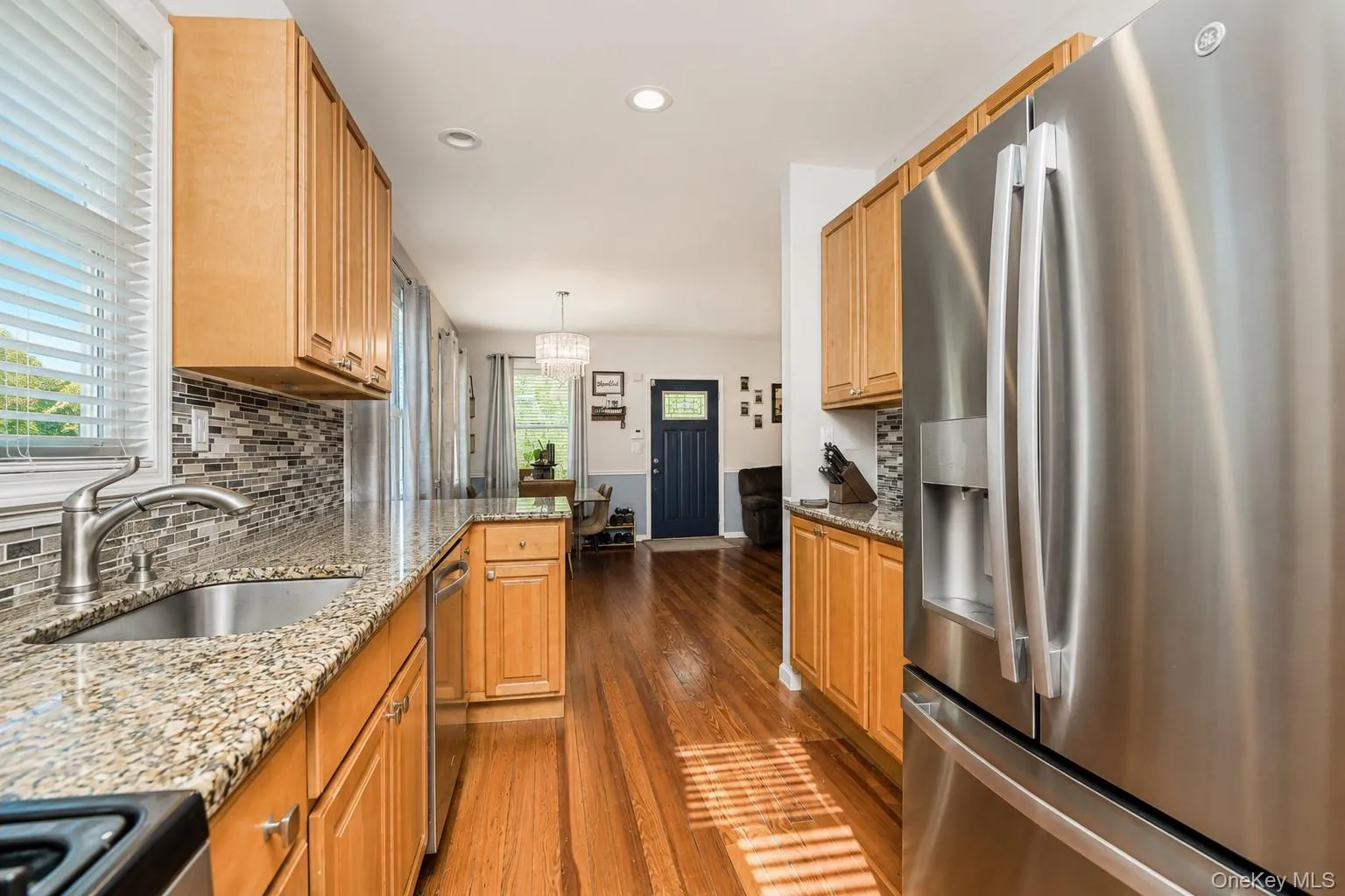 Kitchen featuring wood-finish cabinetry, granite countertops, a stainless steel refrigerator, and a tile backsplash Kitchen featuring wood-finish cabinetry, granite countertops, a stainless steel refrigerator, and a tile backsplash