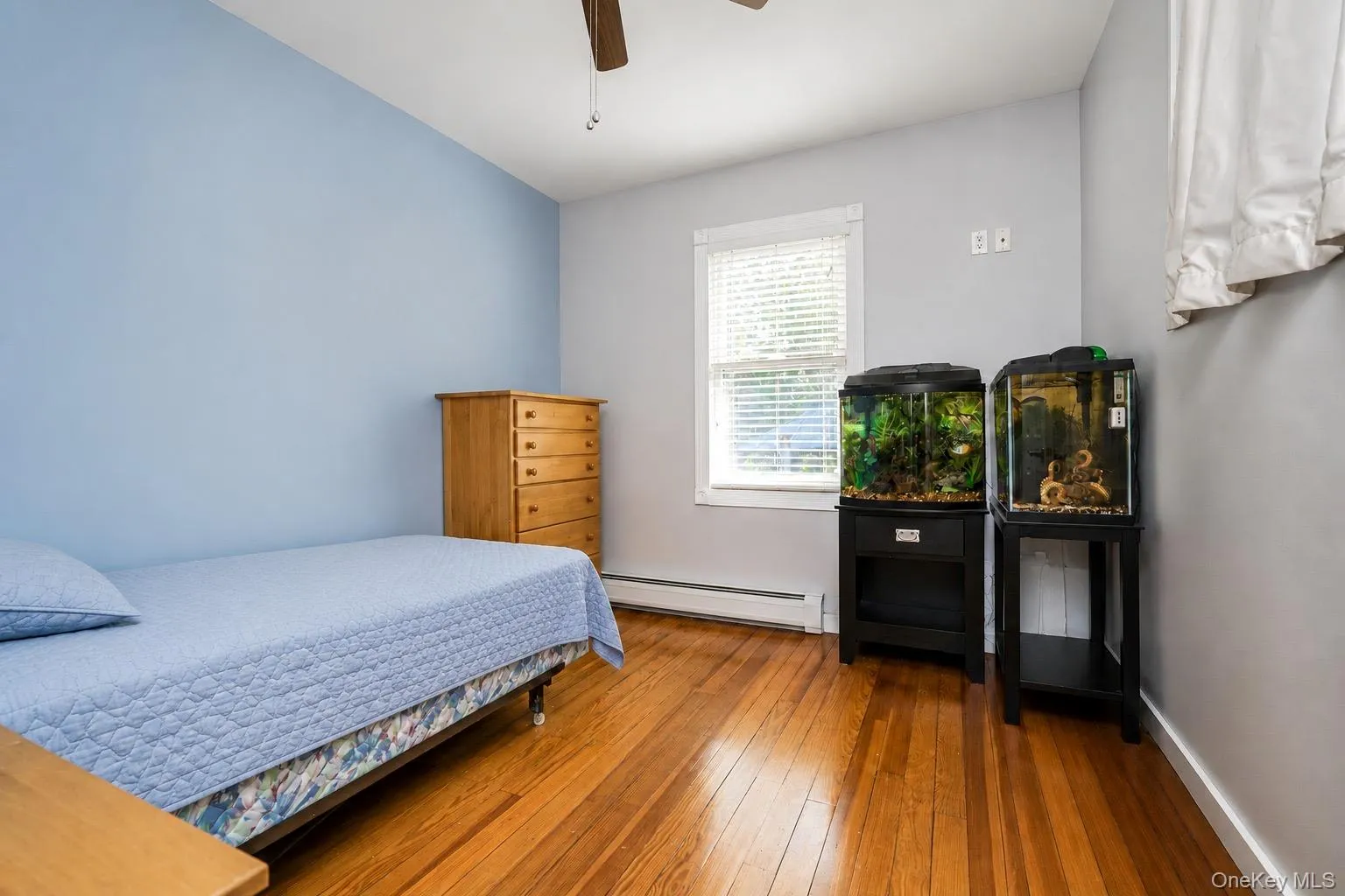 Hardwood flooring throughout featuring a window with blinds, baseboard heating, a ceiling fan, and painted walls Hardwood flooring throughout featuring a window with blinds, baseboard heating, a ceiling fan, and painted walls