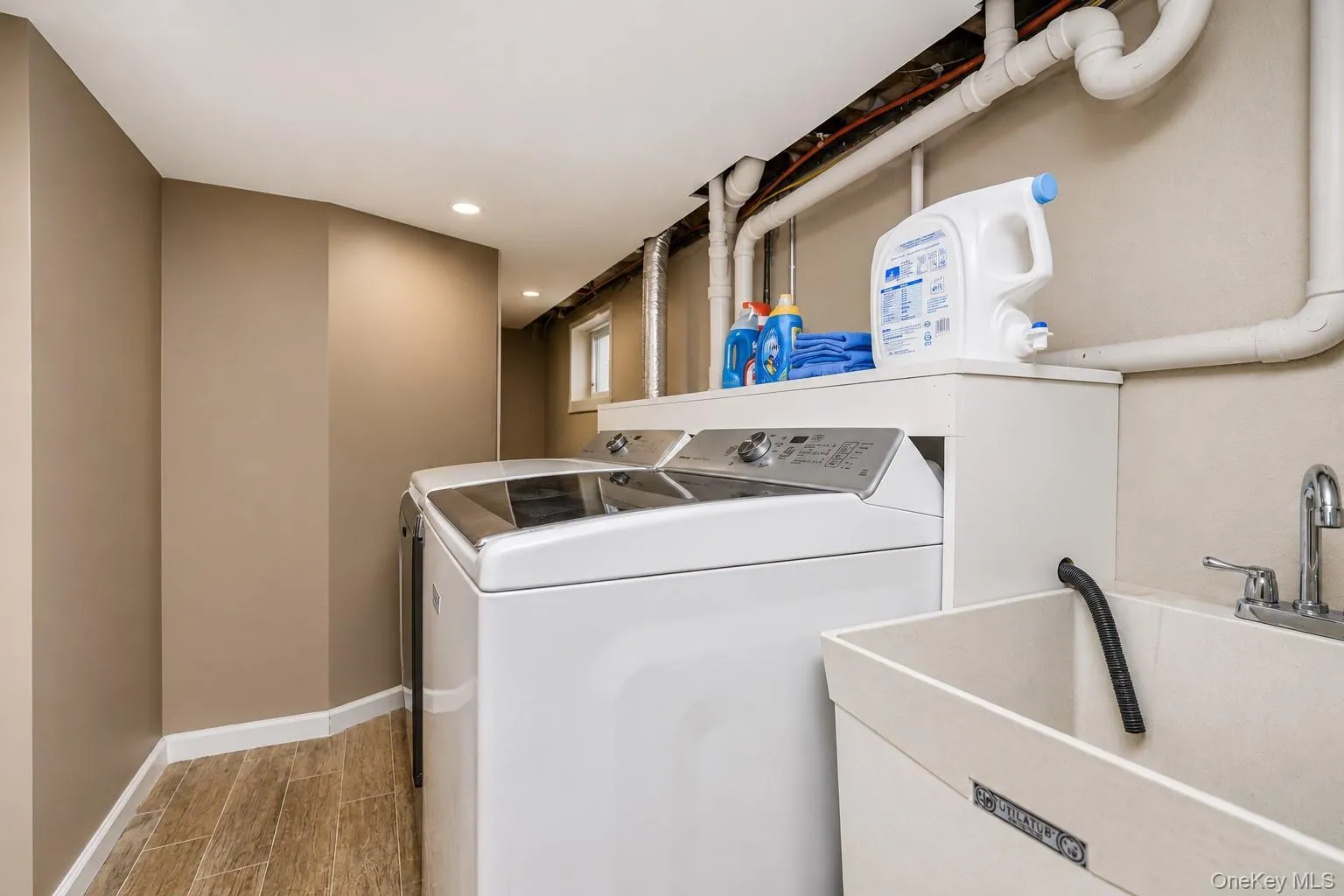 Dedicated laundry area featuring a utility sink with a chrome faucet, wood-finish flooring, and recessed ceiling lighting Dedicated laundry area featuring a utility sink with a chrome faucet, wood-finish flooring, and recessed ceiling lighting