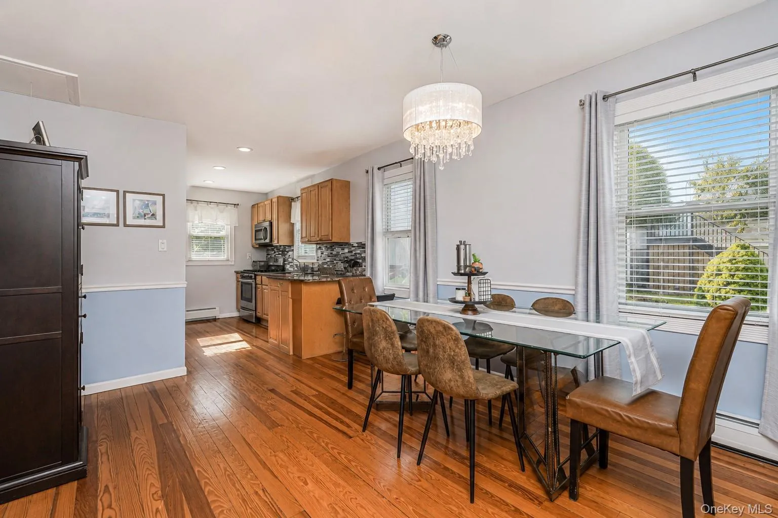 Dining area featuring wood-finish flooring, a contemporary chandelier, and large windows with blinds Dining area featuring wood-finish flooring, a contemporary chandelier, and large windows with blinds