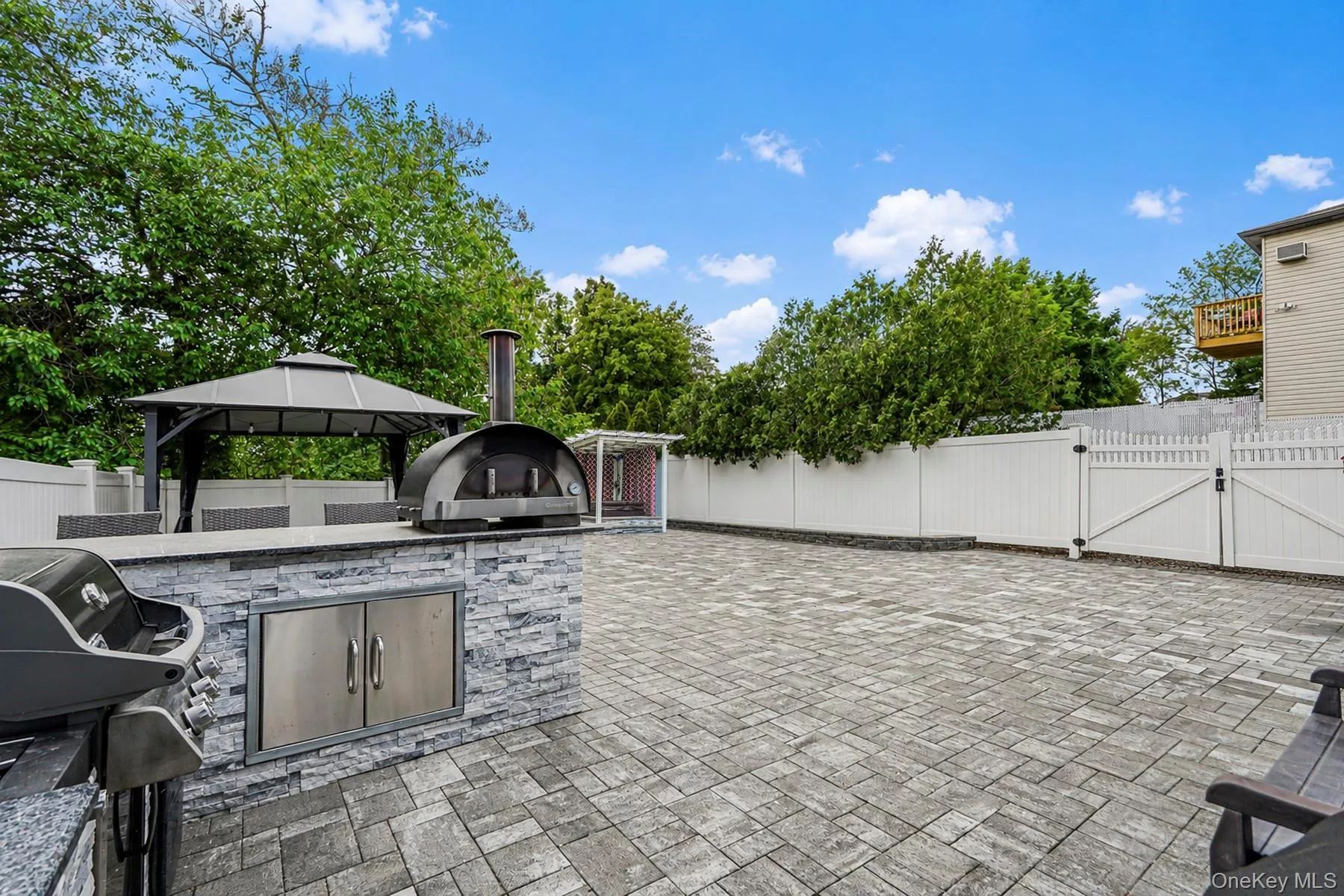 Expansive paved outdoor area featuring a built-in stone veneer outdoor kitchen with stainless steel storage, an outdoor pizza oven, and a separate gazebo Expansive paved outdoor area featuring a built-in stone veneer outdoor kitchen with stainless steel storage, an outdoor pizza oven, and a separate gazebo