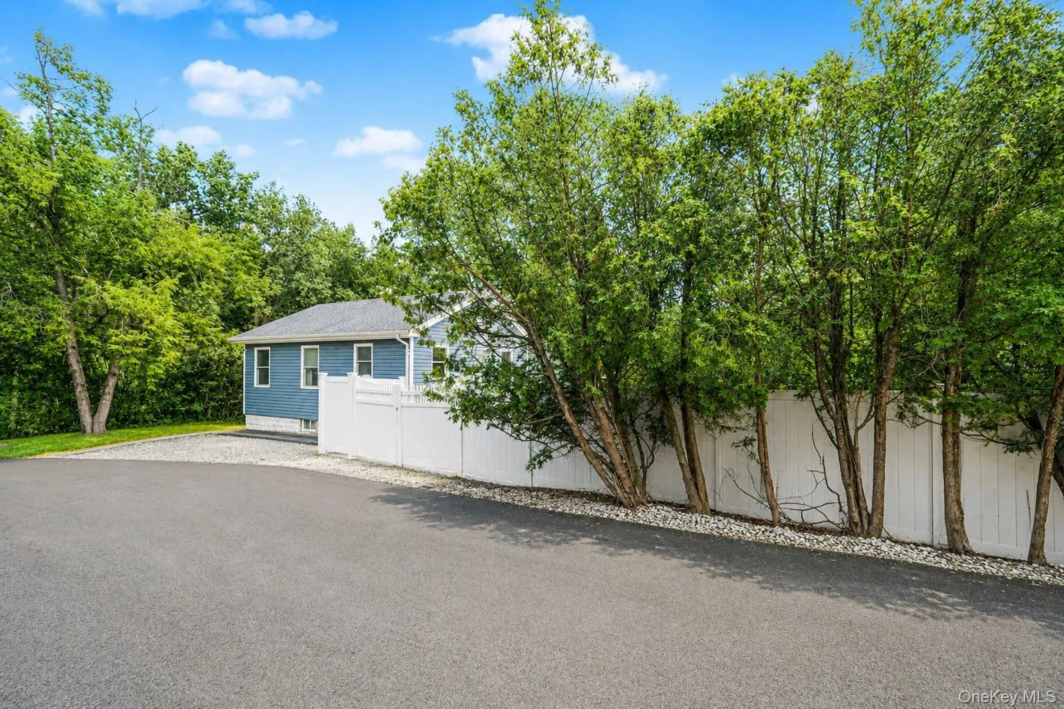 Paved drive leading to a blue siding residence featuring white trim windows and a dark shingle roof Paved drive leading to a blue siding residence featuring white trim windows and a dark shingle roof