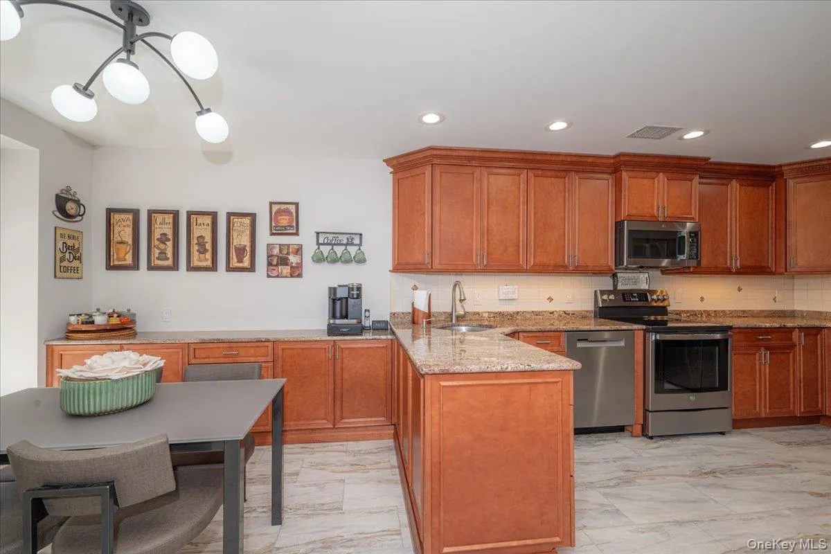 Kitchen featuring wood cabinetry, granite countertops, stainless steel appliances, a tile backsplash, and light-toned tile flooring Kitchen featuring wood cabinetry, granite countertops, stainless steel appliances, a tile backsplash, and light-toned tile flooring