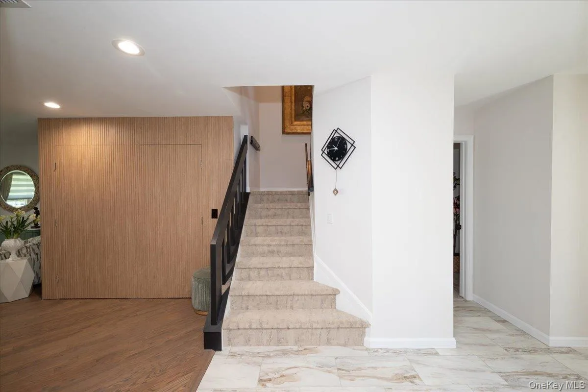 Entryway featuring wood-finish flooring, a carpeted staircase with a dark metal handrail, recessed lighting, and light-toned wall finishes Entryway featuring wood-finish flooring, a carpeted staircase with a dark metal handrail, recessed lighting, and light-toned wall finishes