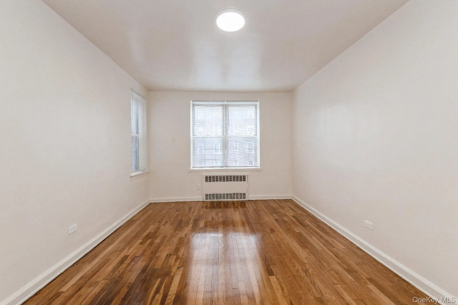 Empty room with wood-type flooring, baseboards, and radiator Empty room with wood-type flooring, baseboards, and radiator