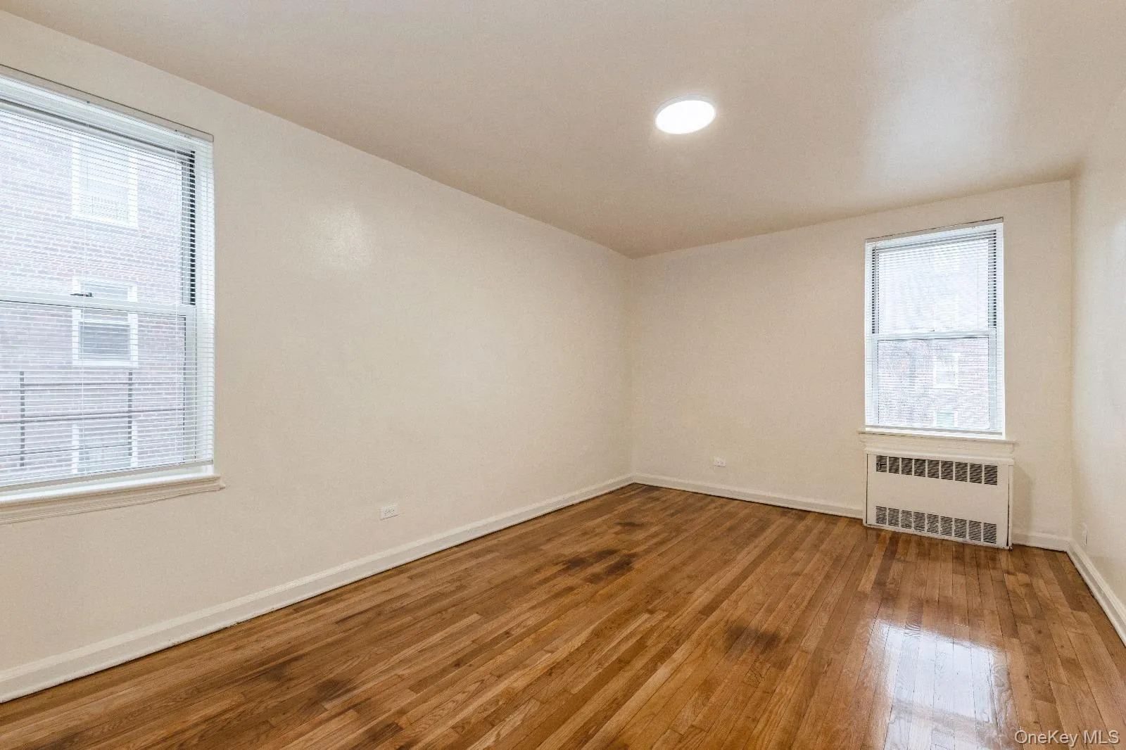 Empty room featuring radiator heating unit, baseboards, and wood finished floors Empty room featuring radiator heating unit, baseboards, and wood finished floors