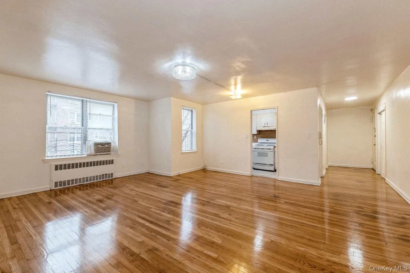 Unfurnished living room featuring radiator, light wood-style floors, and baseboards Unfurnished living room featuring radiator, light wood-style floors, and baseboards