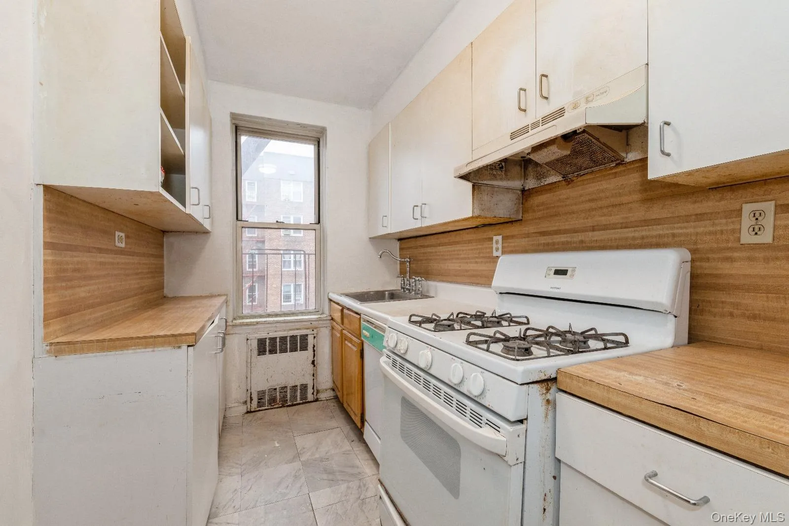 Kitchen featuring a sink, radiator heating unit, under cabinet range hood, marble finish floor, and white appliances Kitchen featuring a sink, radiator heating unit, under cabinet range hood, marble finish floor, and white appliances