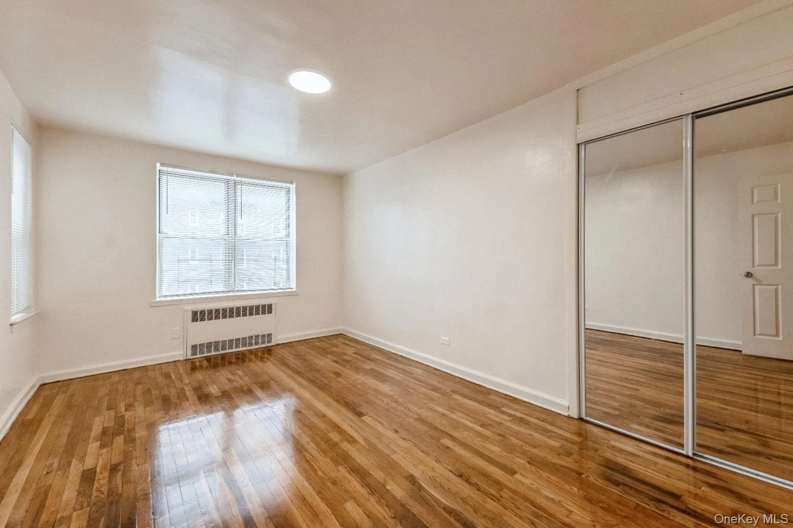Unfurnished bedroom featuring baseboards, a closet, radiator heating unit, and hardwood / wood-style floors Unfurnished bedroom featuring baseboards, a closet, radiator heating unit, and hardwood / wood-style floors