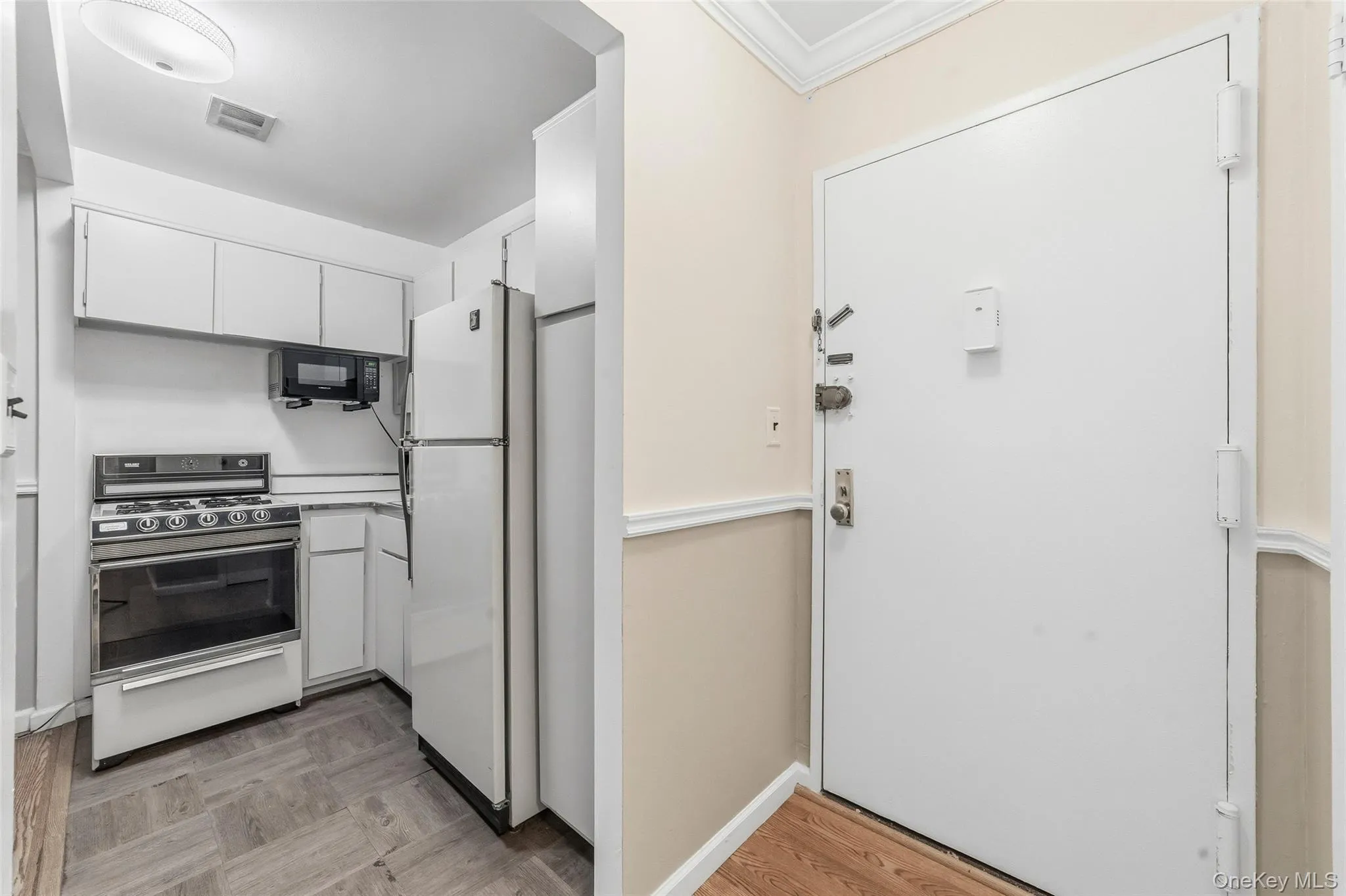 Compact kitchen featuring white cabinetry, a white refrigerator, a microwave, a range with an oven, and wood-finish flooring Compact kitchen featuring white cabinetry, a white refrigerator, a microwave, a range with an oven, and wood-finish flooring
