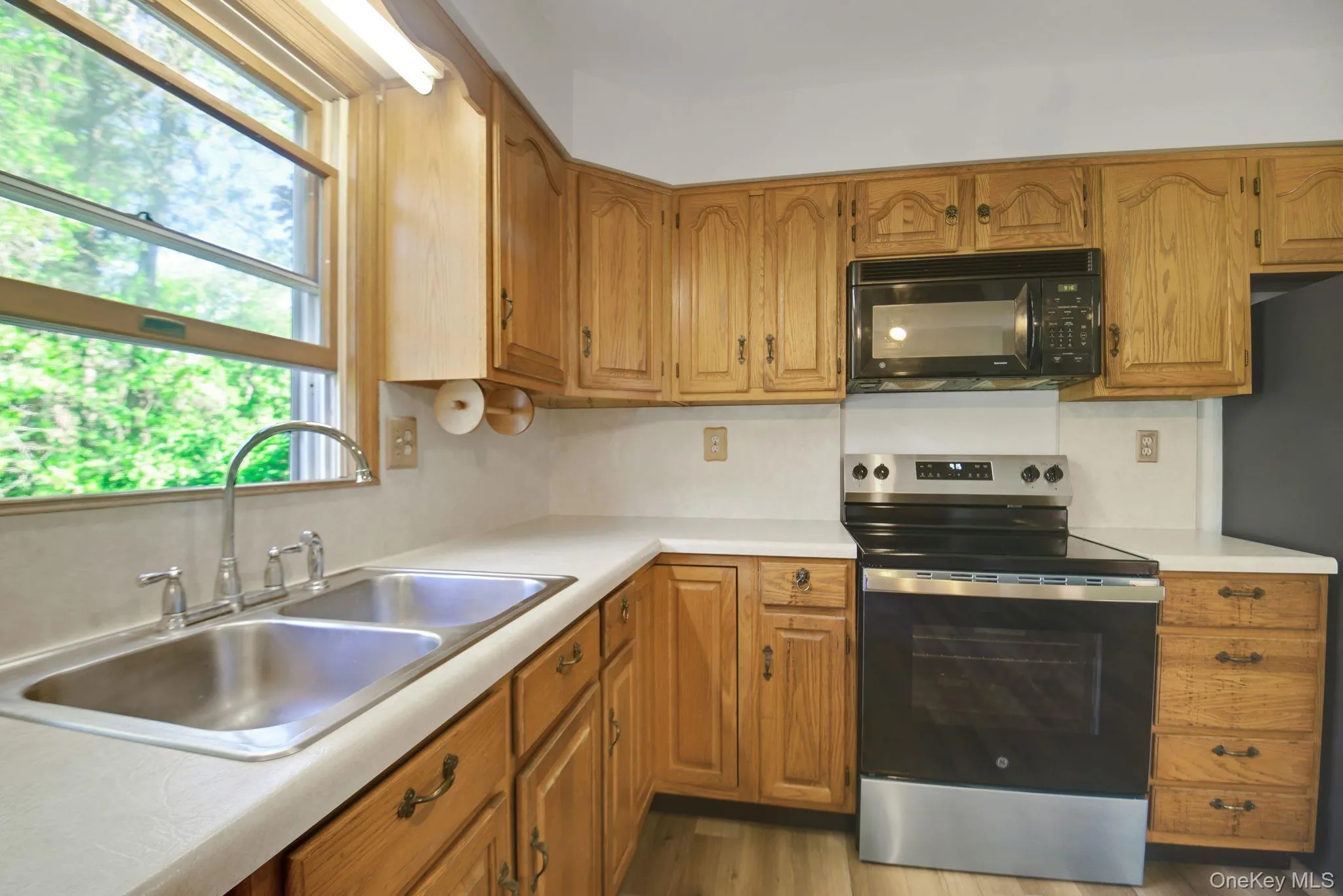 Kitchen featuring wood cabinetry, laminate countertops, a stainless steel double basin sink, a modern black and stainless steel range, and an over-the-range microwave Kitchen featuring wood cabinetry, laminate countertops, a stainless steel double basin sink, a modern black and stainless steel range, and an over-the-range microwave