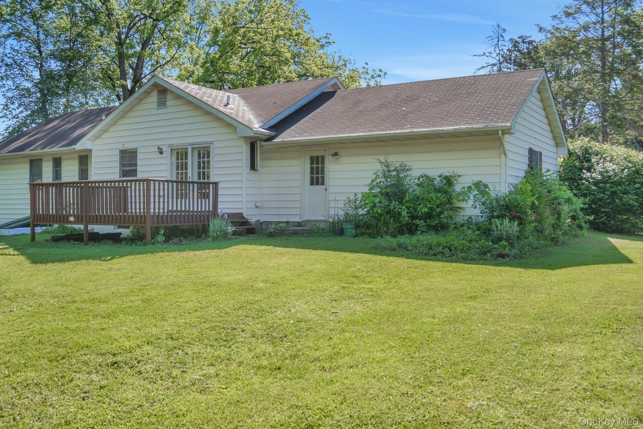 Expansive green lawn with a white siding exterior, brown wooden deck, double glass panel doors, and a side entry door Expansive green lawn with a white siding exterior, brown wooden deck, double glass panel doors, and a side entry door