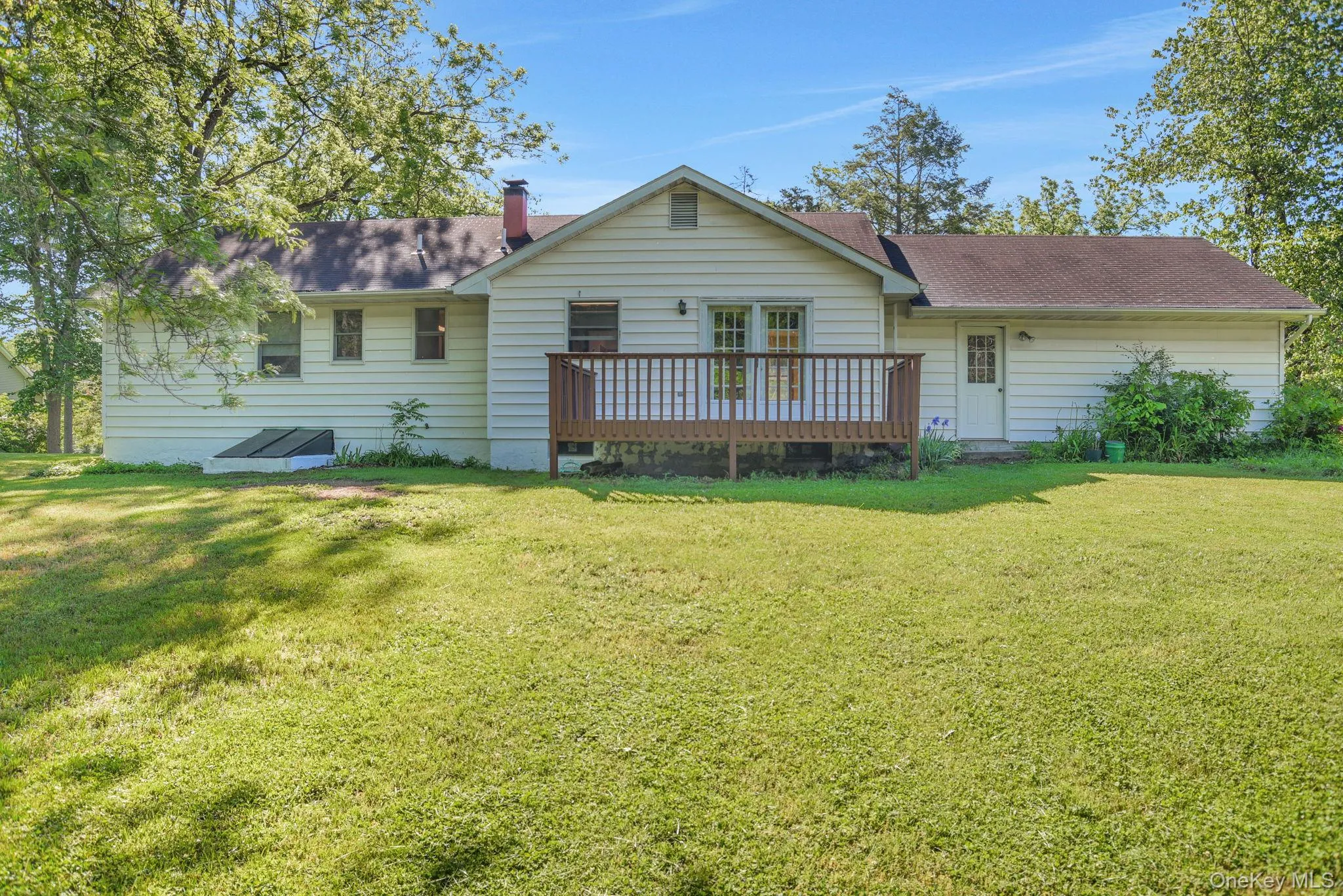 Rear exterior featuring white siding, a wooden deck, and a spacious grassy area Rear exterior featuring white siding, a wooden deck, and a spacious grassy area
