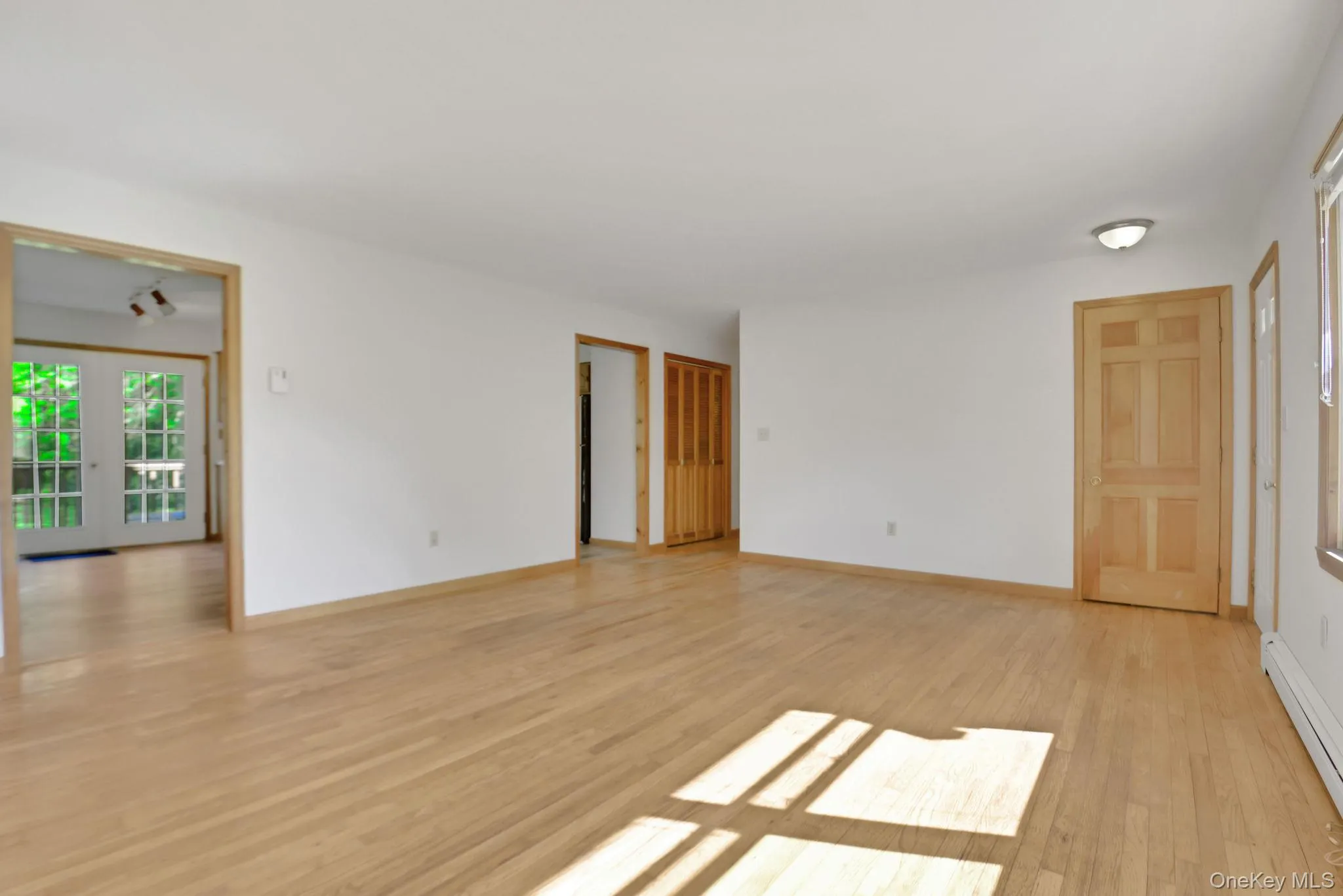 Spacious room featuring light wood-finish flooring, white walls, and natural wood trim throughout Spacious room featuring light wood-finish flooring, white walls, and natural wood trim throughout