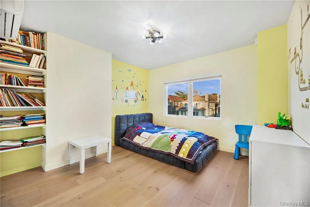 Light wood-finish flooring with built-in shelving, a large window, and a wall-mounted air conditioning unit Light wood-finish flooring with built-in shelving, a large window, and a wall-mounted air conditioning unit