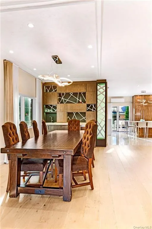 Bright dining area with light wood-finish flooring, recessed lighting, and a modern linear chandelier Bright dining area with light wood-finish flooring, recessed lighting, and a modern linear chandelier