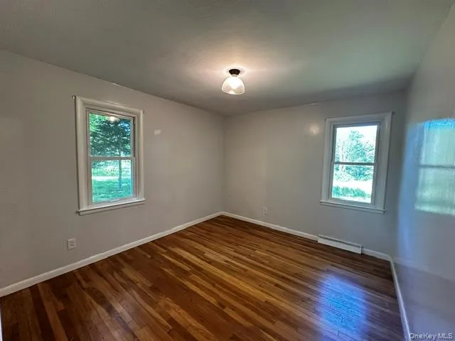 Hardwood flooring, painted walls, window with trim, and a ceiling-mounted light fixture Hardwood flooring, painted walls, window with trim, and a ceiling-mounted light fixture