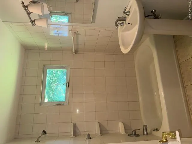 Bathroom featuring a built-in bathtub with shower, wall-mounted showerhead, and tiled surround Bathroom featuring a built-in bathtub with shower, wall-mounted showerhead, and tiled surround
