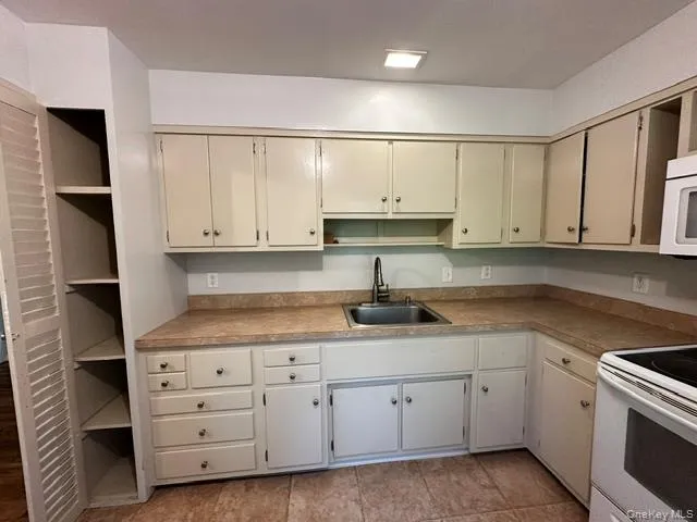 L-shaped kitchen featuring cream cabinetry, and a built-in pantry with louvered doors L-shaped kitchen featuring cream cabinetry, and a built-in pantry with louvered doors