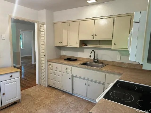 Functional kitchen featuring ample cabinetry, a stainless steel sink with a gooseneck faucet, an electric cooktop, a built-in microwave, and tile flooring Functional kitchen featuring ample cabinetry, a stainless steel sink with a gooseneck faucet, an electric cooktop, a built-in microwave, and tile flooring