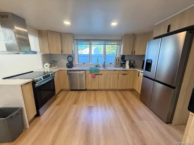 Kitchen with appliances with stainless steel finishes, wall chimney exhaust hood, light wood-style floors, light brown cabinetry, and recessed lighting Kitchen with appliances with stainless steel finishes, wall chimney exhaust hood, light wood-style floors, light brown cabinetry, and recessed lighting