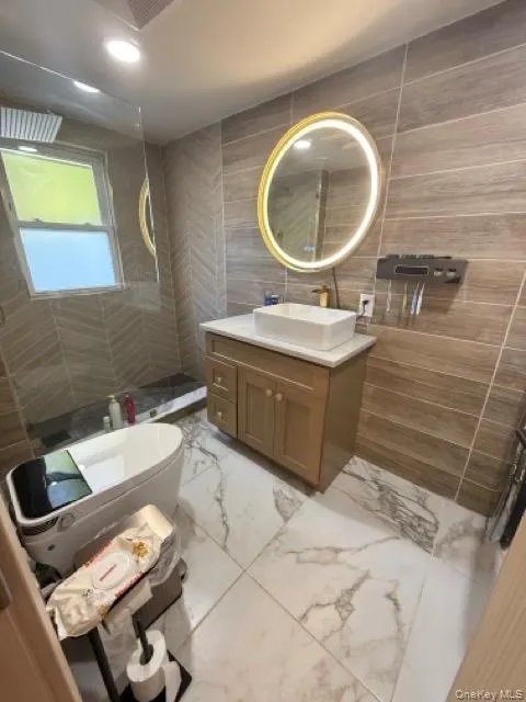Full bathroom with tile walls, vanity, light marble finish floors, a tile shower, and recessed lighting Full bathroom with tile walls, vanity, light marble finish floors, a tile shower, and recessed lighting
