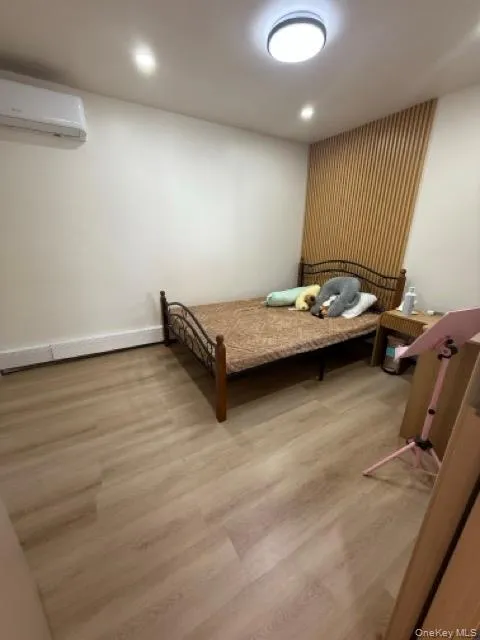 Bedroom featuring wood finished floors, a wall mounted AC, recessed lighting, and a baseboard radiator Bedroom featuring wood finished floors, a wall mounted AC, recessed lighting, and a baseboard radiator