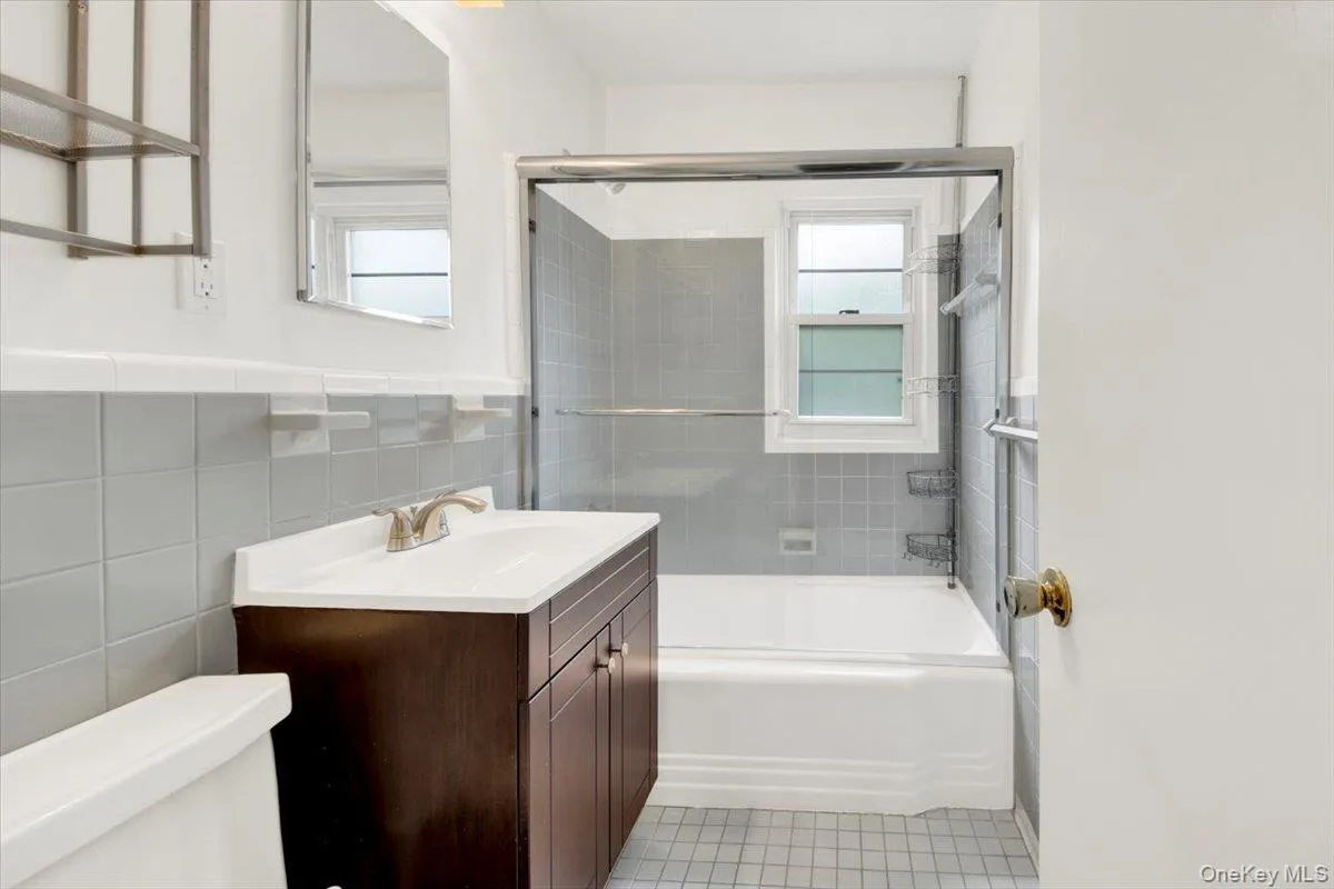 Bathroom featuring vanity, enclosed tub/shower combo, tiled wall, tile patterned floors & wainscoted wall Bathroom featuring vanity, enclosed tub/shower combo, tiled wall, tile patterned floors & wainscoted wall