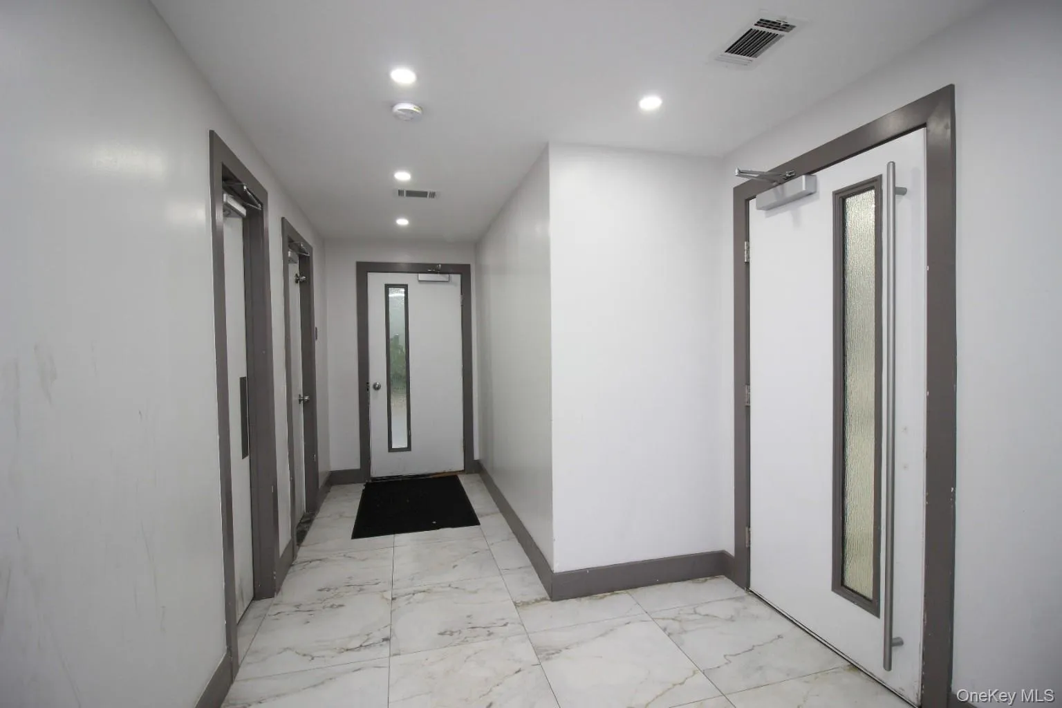 Hallway featuring white walls, gray trim, and marble-patterned floor tiles Hallway featuring white walls, gray trim, and marble-patterned floor tiles