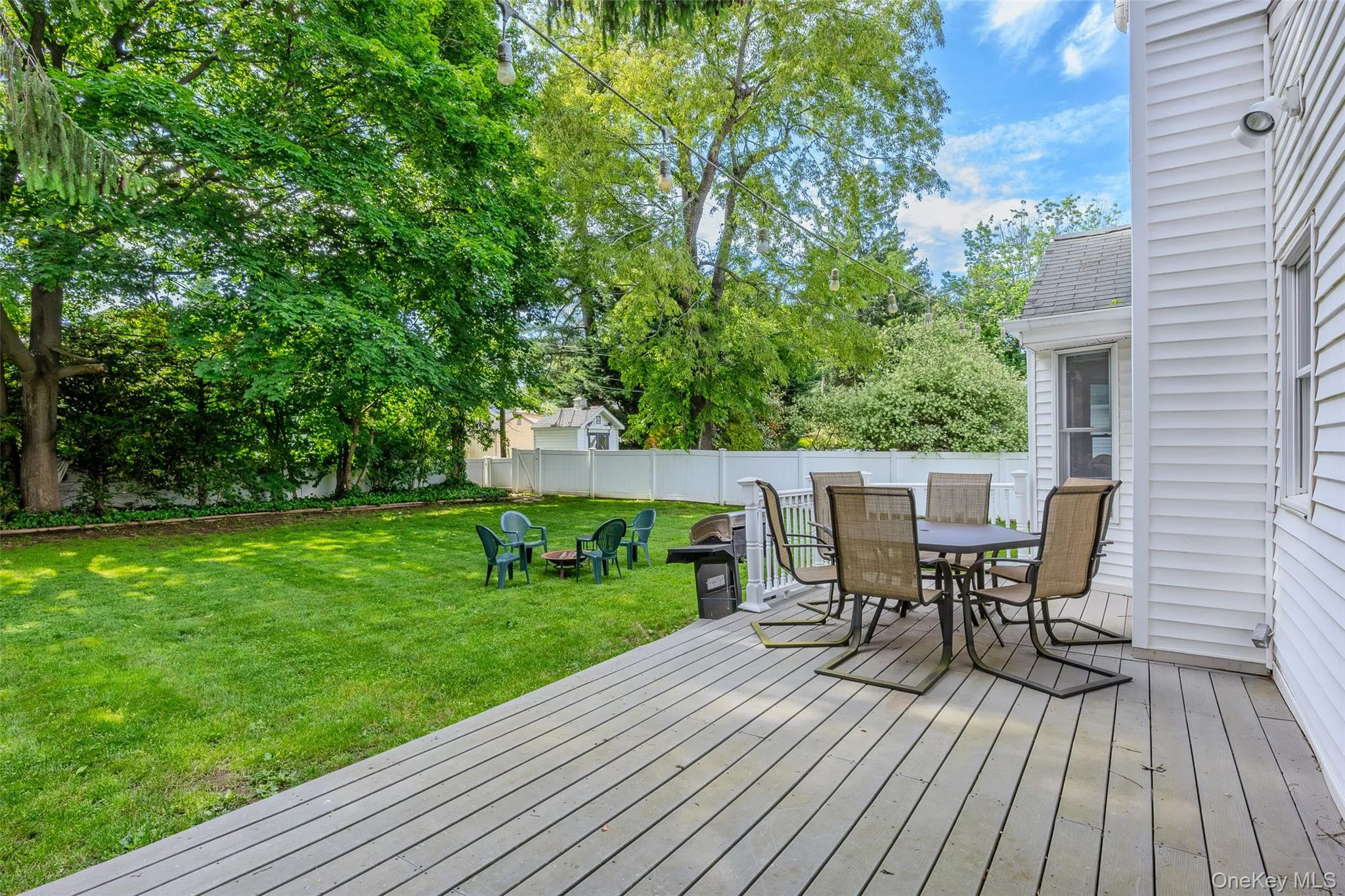 Spacious wooden deck overlooking a manicured lawn, framed by mature trees and a white privacy fence Spacious wooden deck overlooking a manicured lawn, framed by mature trees and a white privacy fence
