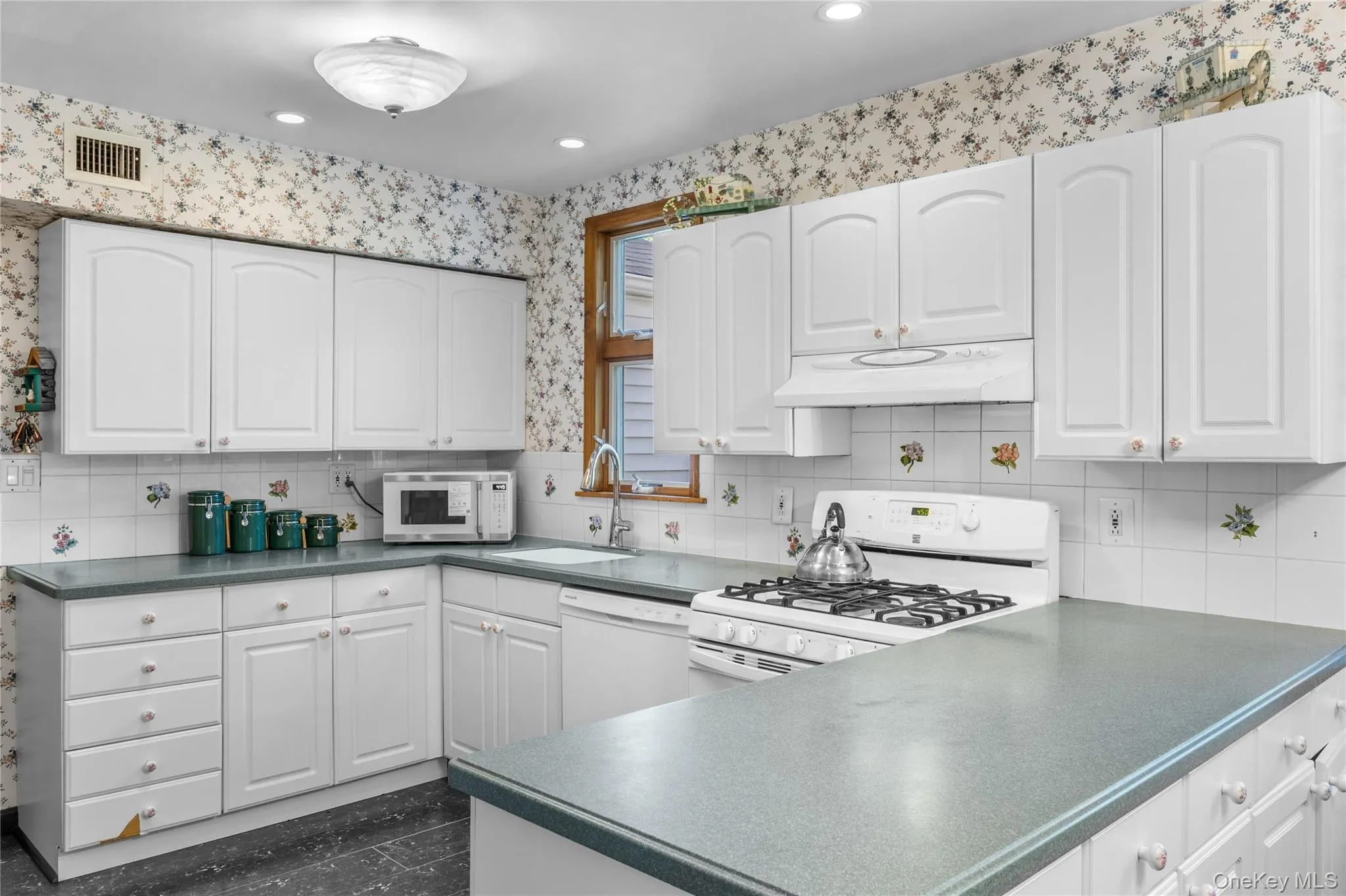 Kitchen featuring white cabinetry, a gas range with overhead exhaust and ample countertop space Kitchen featuring white cabinetry, a gas range with overhead exhaust and ample countertop space