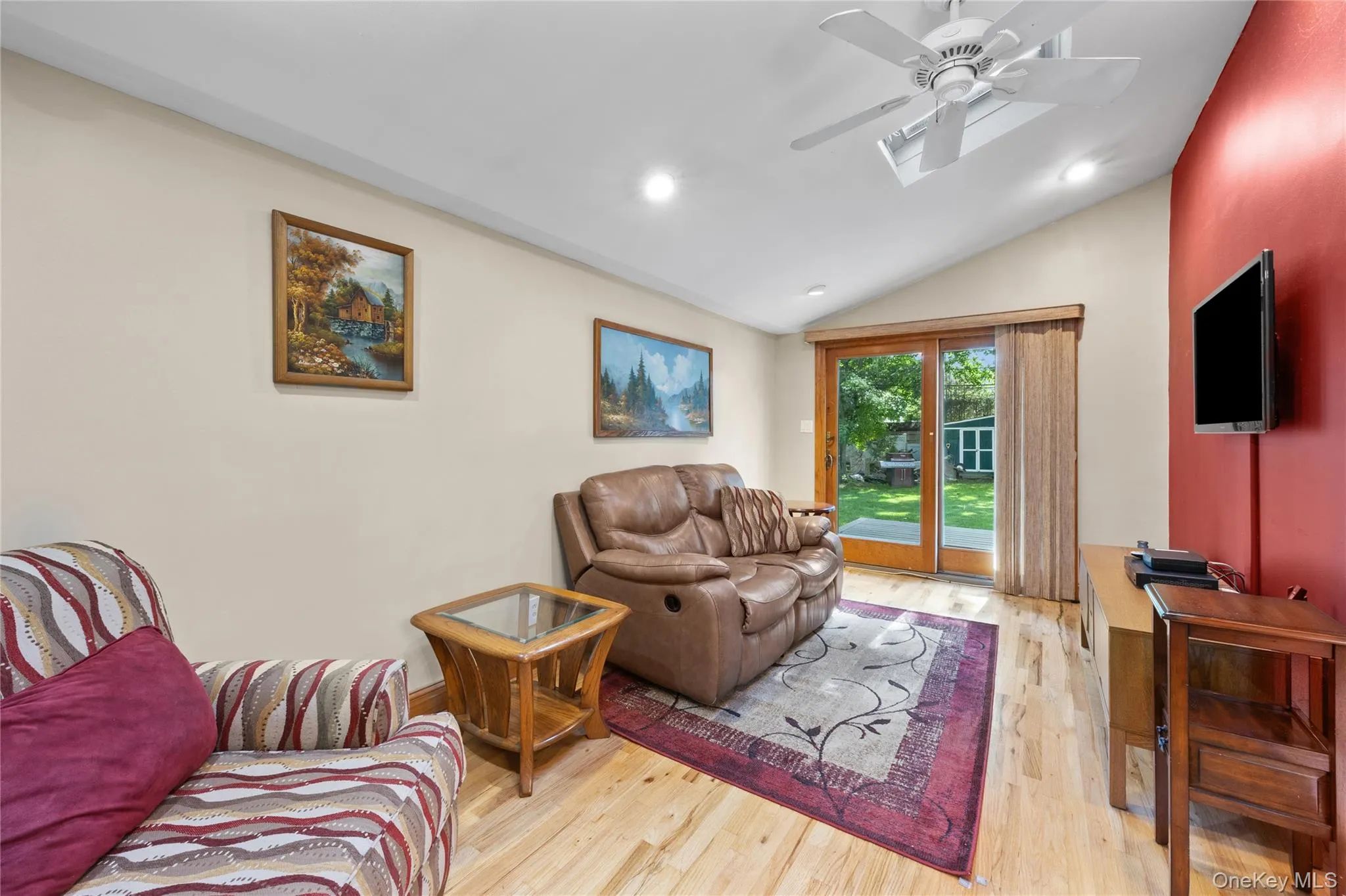 Vaulted ceiling living area featuring light wood-finish flooring, recessed lighting, skylight and sliding door to deck Vaulted ceiling living area featuring light wood-finish flooring, recessed lighting, skylight and sliding door to deck
