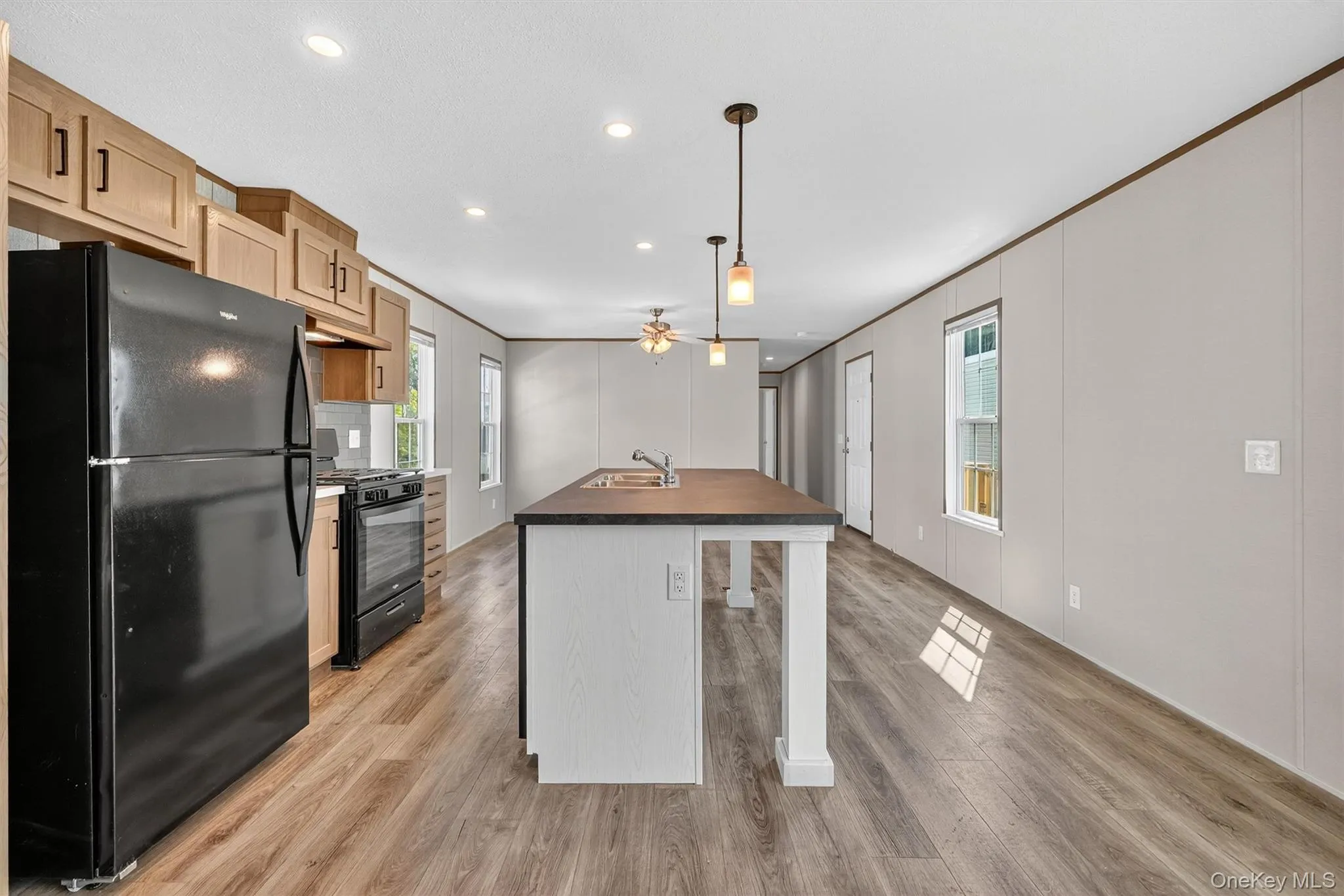 Kitchen with black appliances, a kitchen island with sink, light wood finished floors, dark countertops, and crown molding Kitchen with black appliances, a kitchen island with sink, light wood finished floors, dark countertops, and crown molding
