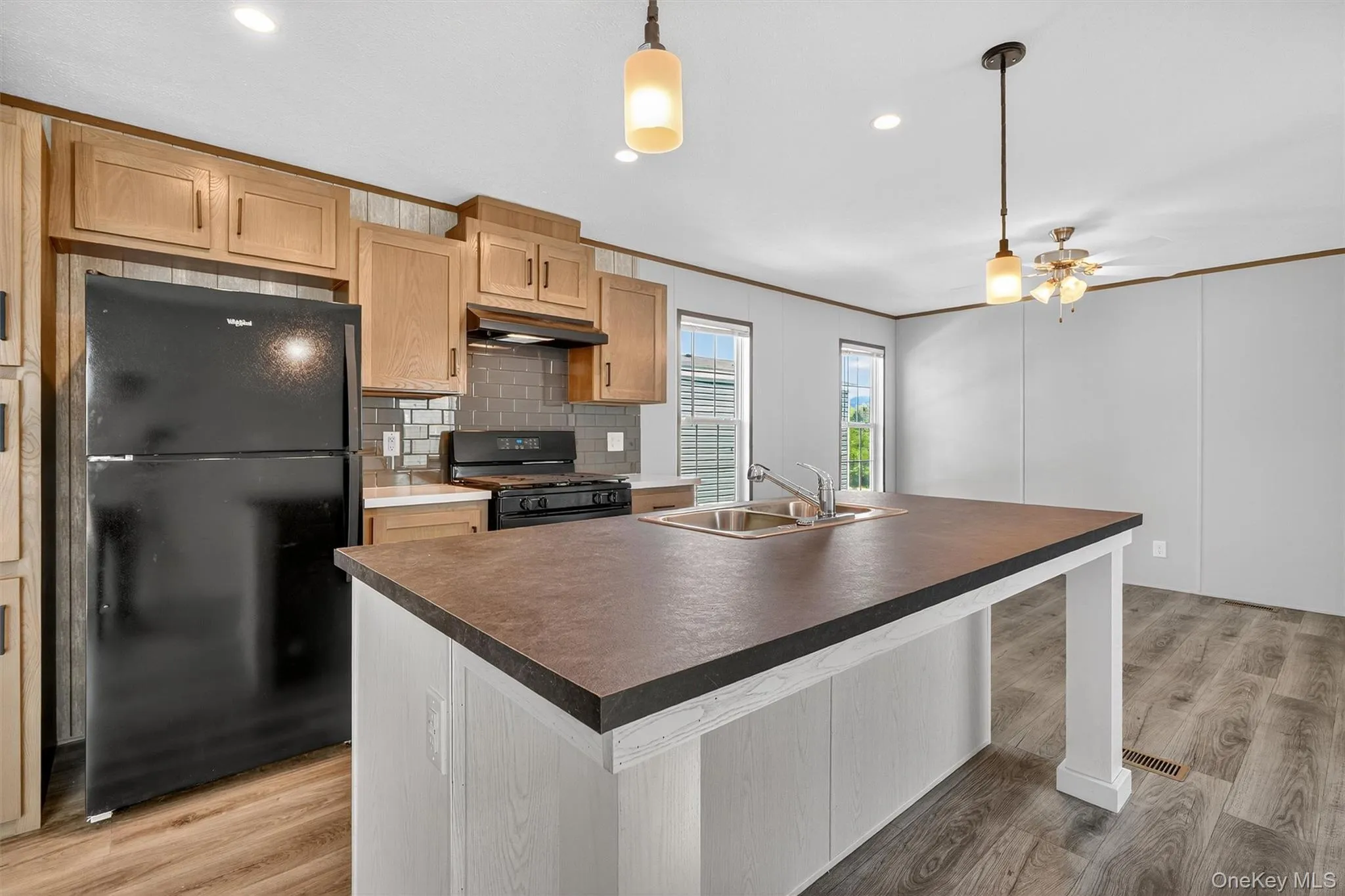 Kitchen featuring an island with sink, black appliances, tasteful backsplash, light wood-style flooring, and pendant lighting Kitchen featuring an island with sink, black appliances, tasteful backsplash, light wood-style flooring, and pendant lighting