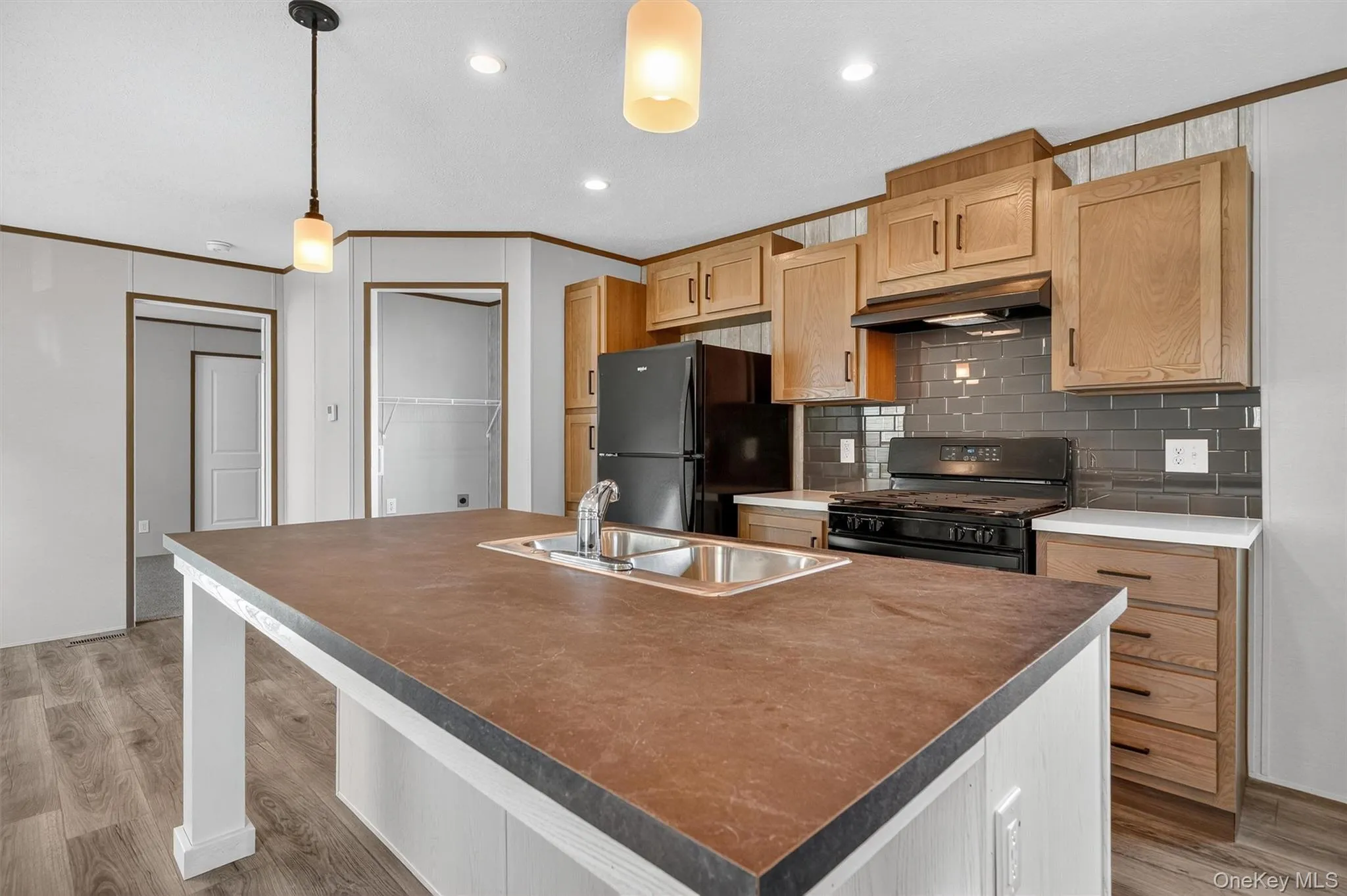 Kitchen featuring backsplash, pendant lighting, black appliances, ornamental molding, and light wood-type flooring Kitchen featuring backsplash, pendant lighting, black appliances, ornamental molding, and light wood-type flooring