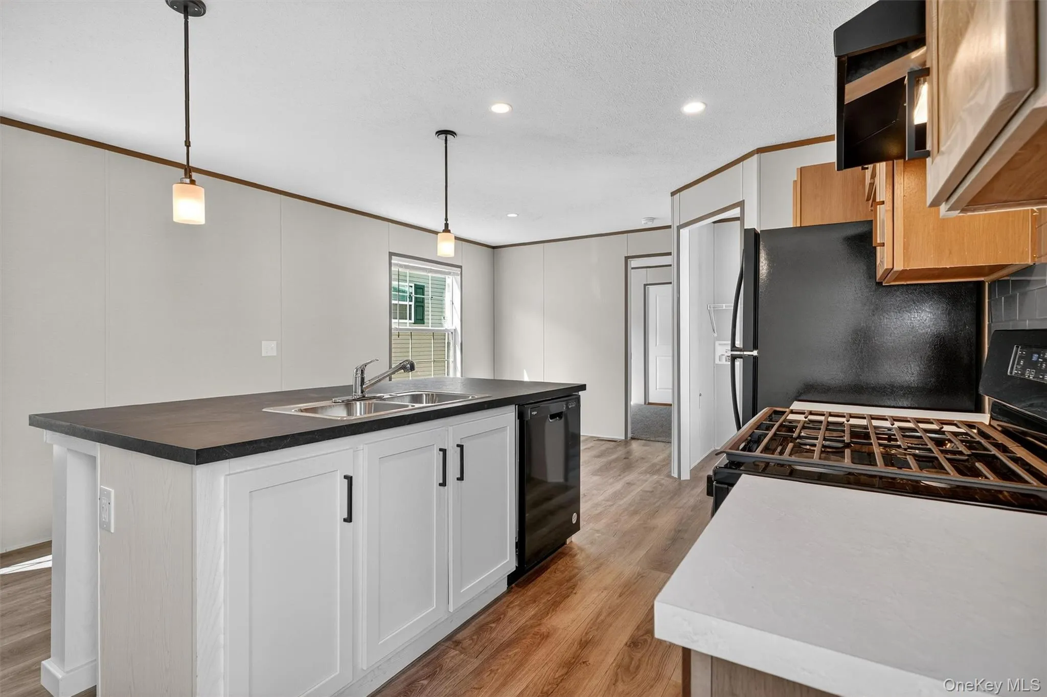 Kitchen with pendant lighting, a kitchen island with sink, dark countertops, gas range, and light wood-type flooring Kitchen with pendant lighting, a kitchen island with sink, dark countertops, gas range, and light wood-type flooring